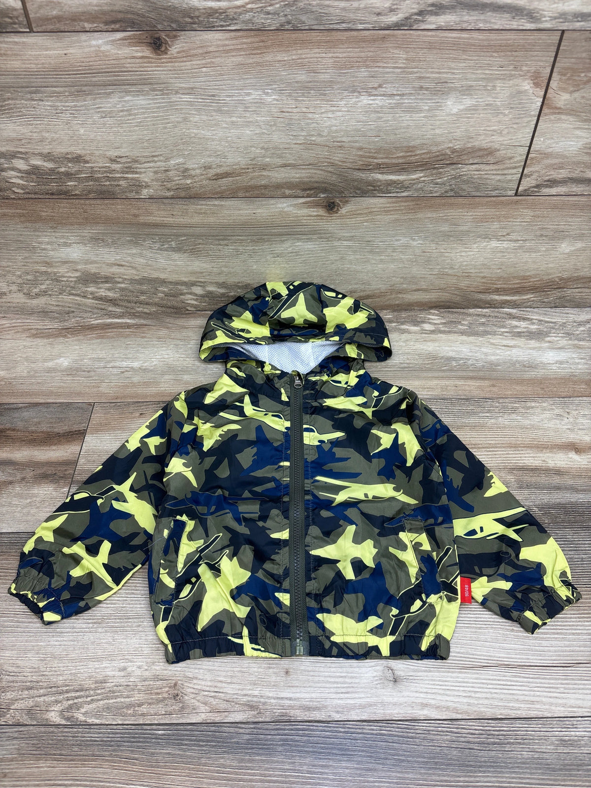 Front view of a green camo airplane windbreaker jacket in size 18 months, showcasing hood, front zipper, pockets, and elastic cuffs