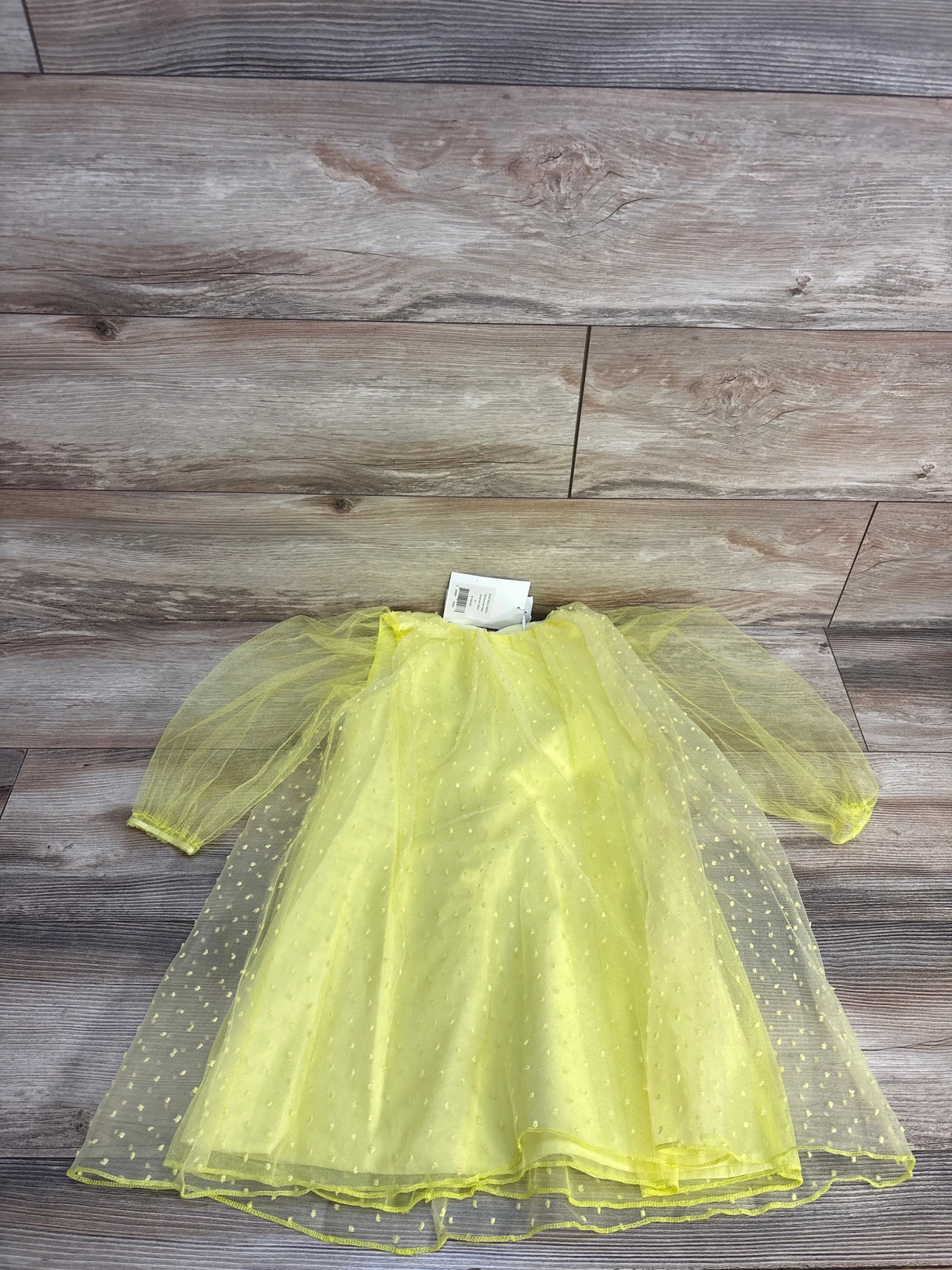 Yellow tulle baby dress with polka dots, long sleeves, laid on wood floor