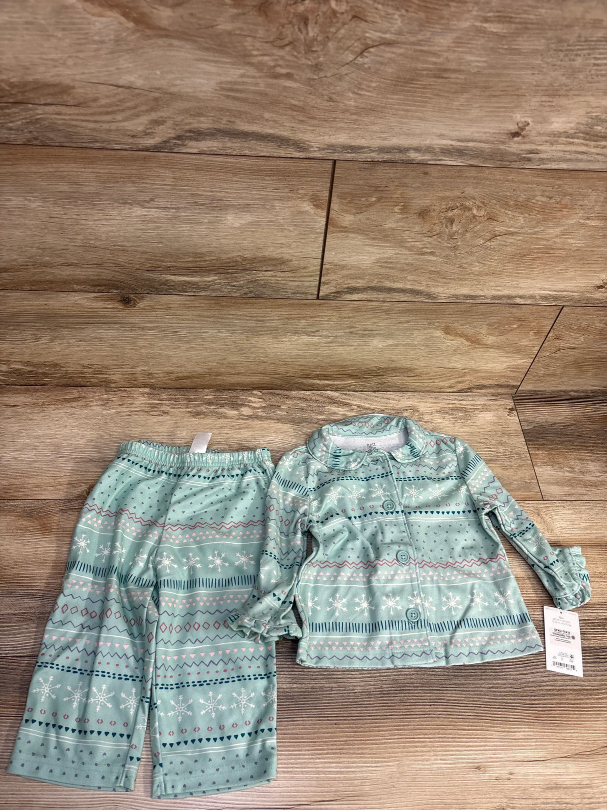 Mint green toddler pajama set with snowflake pattern, long sleeves and pants on wood floor