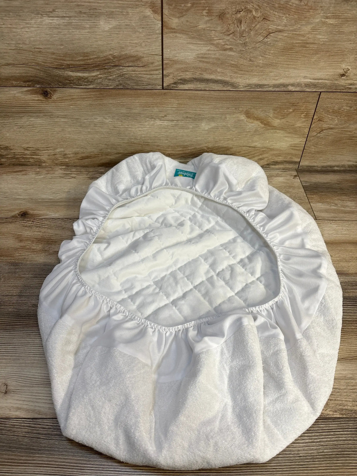 White quilted fitted changing pad cover for baby, elastic edges, on wood floor