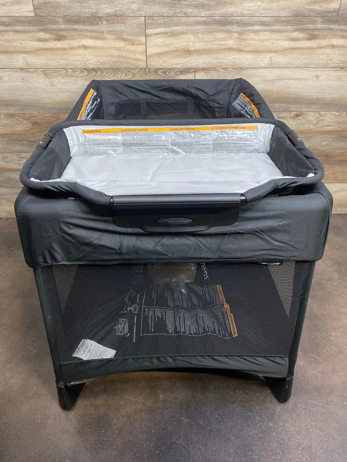 Front, slightly elevated view of 4moms Breeze Plus playard in black showing attached changing station and mesh sides against wood-paneled background