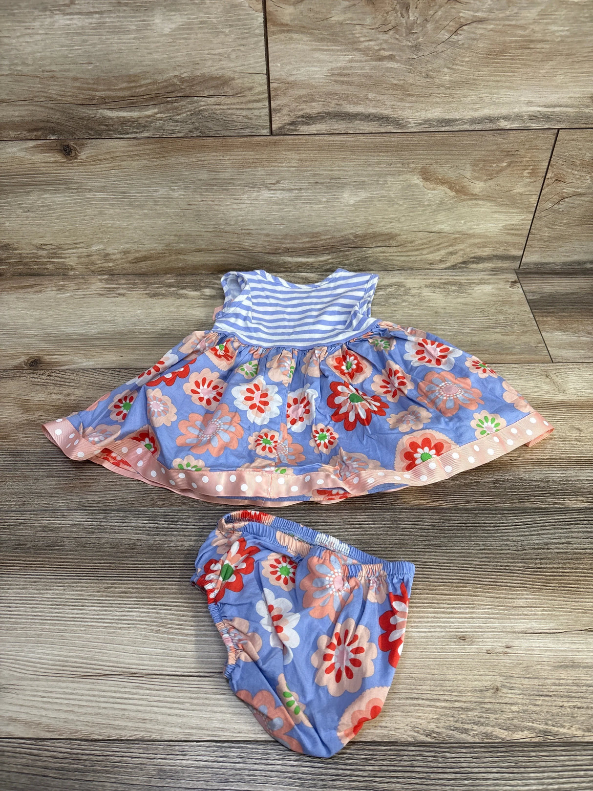 Top view of 2-piece sleeveless dress and bloomers set with blue floral print, striped top and pink trim on wood floor
