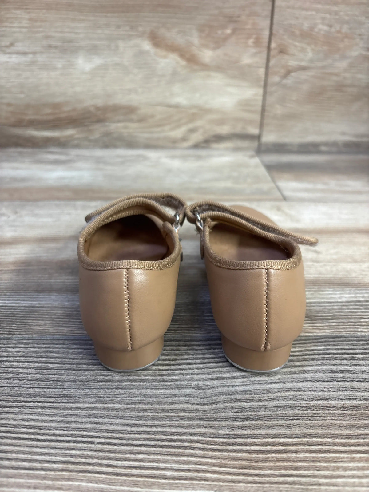 Rear view of tan tap shoes in size 7C showcasing stitched heel panels and low heels on a wood grain floor