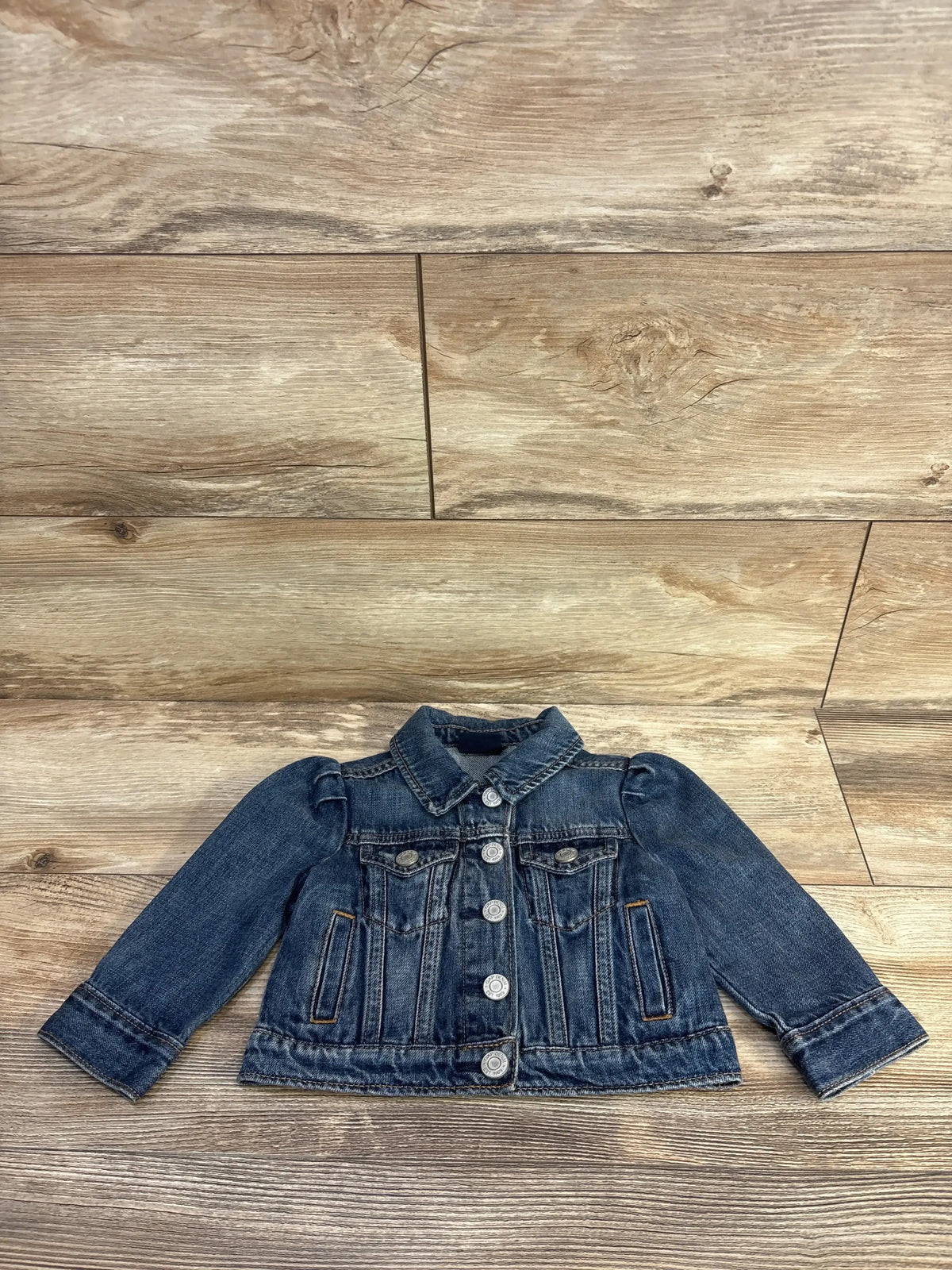 Front view of Baby Gap x Disney Minnie Mouse Icon Denim Jacket size 12-18m in medium-wash blue with puff sleeves and button front on wood plank floor