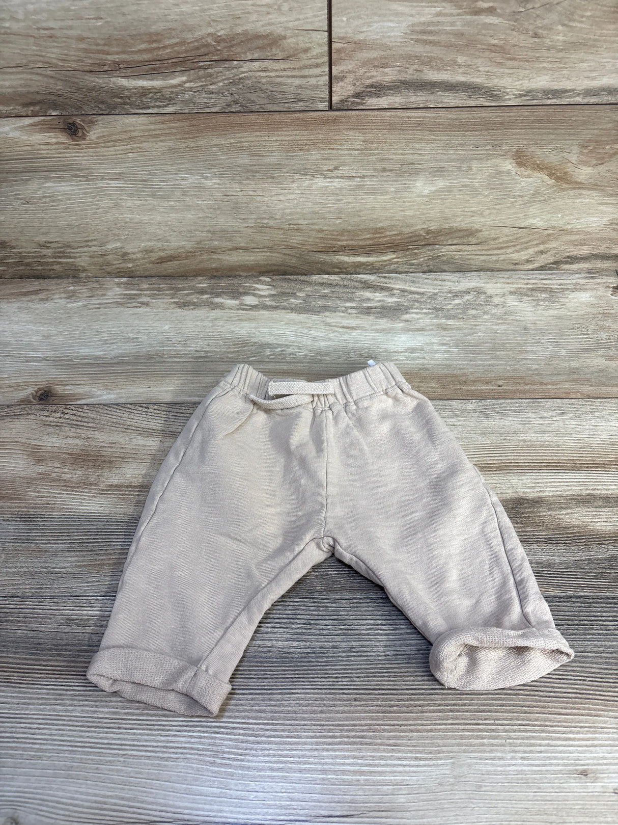 Flat lay of tan H&M drawstring joggers size 6M showing elastic waistband and rolled cuffs on wood background