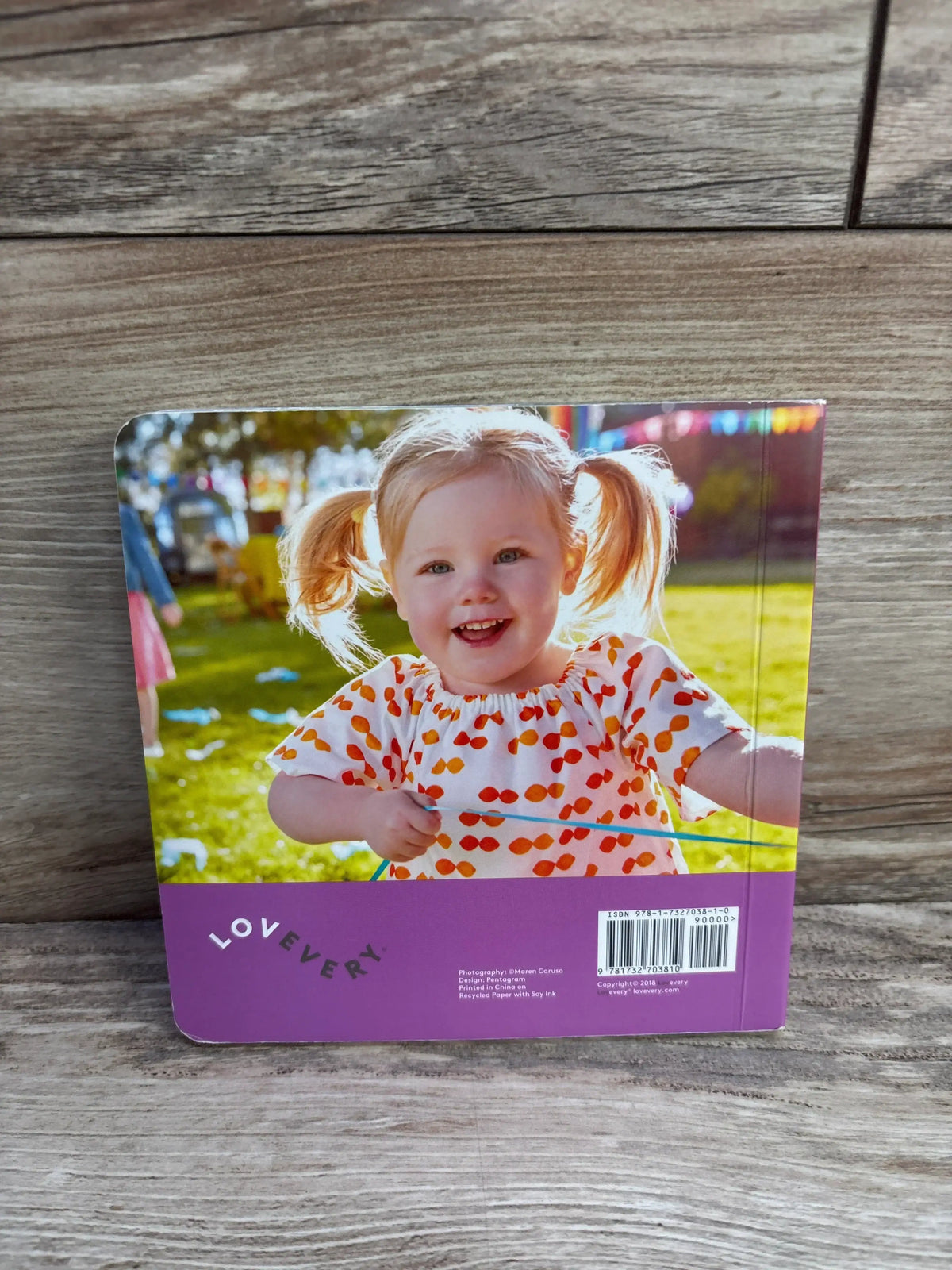 Back of Lovevery Graham Turns Two board book showcasing a smiling toddler and purple band with LOVEVERY logo on wood