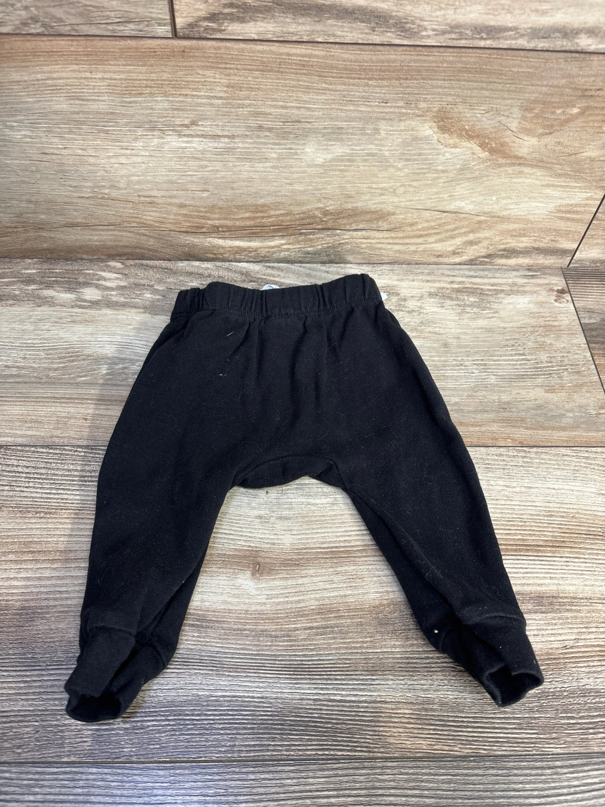 Front view of black drawstring pants showcasing a relaxed fit and adjustable waist on a wood-look floor