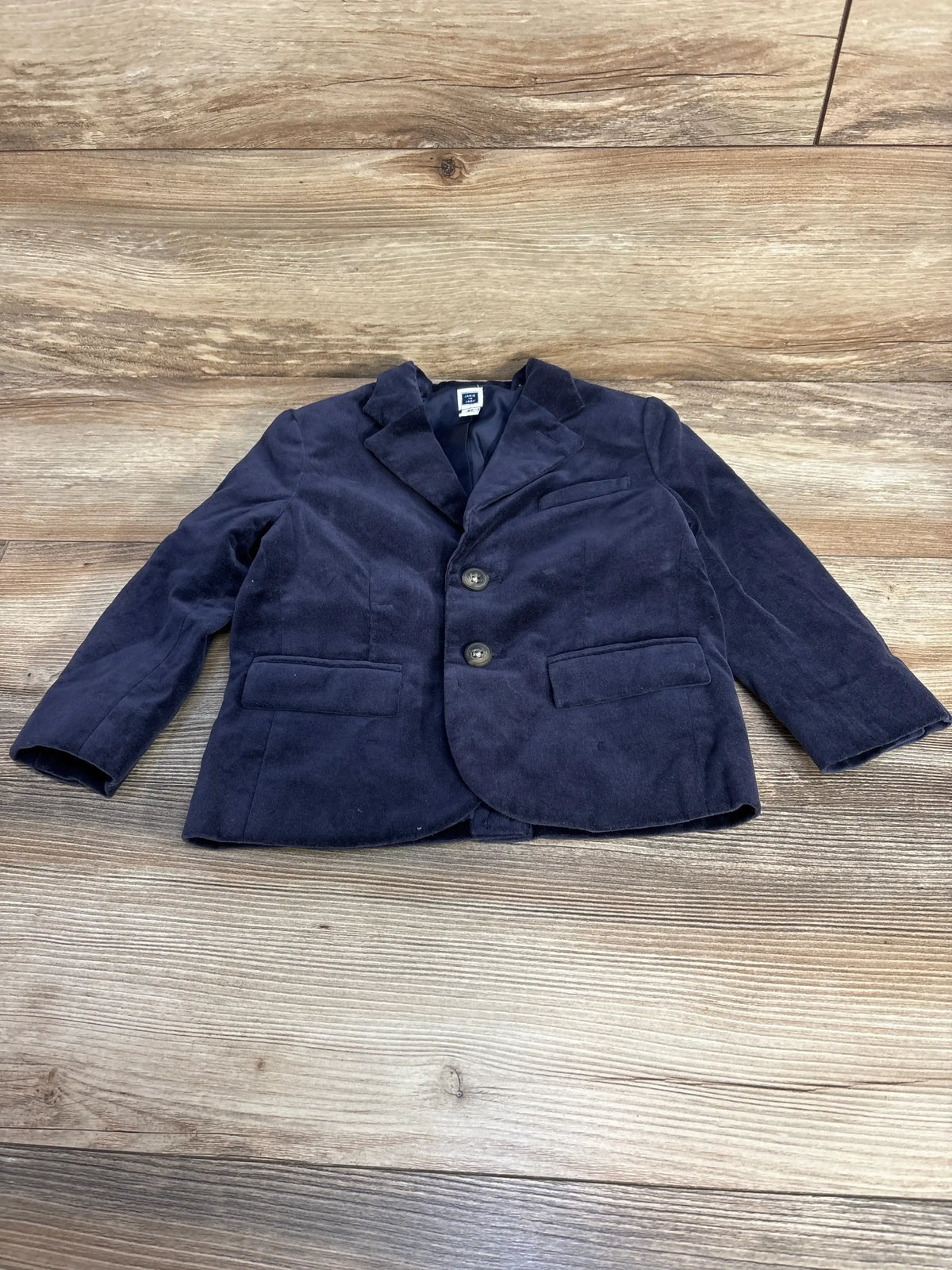 Front flat lay of Janie & Jack dark marine velvet blazer, two-button front, notch lapel, flap pockets on light wood floor