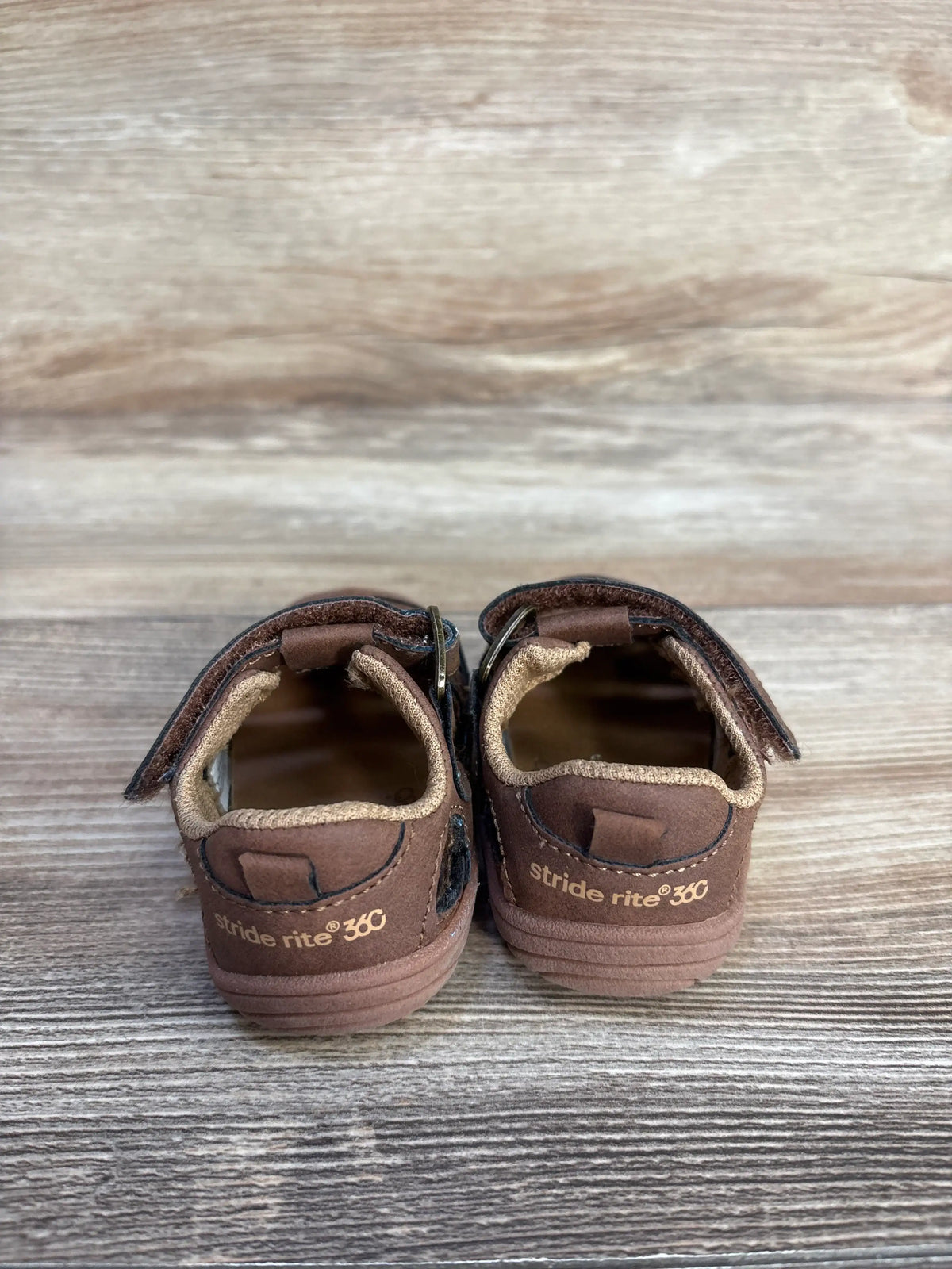 Rear view of Stride Rite Amos 3.0 fisherman sandals showcasing brown closed-toe uppers and ankle straps on a wood-grain surface
