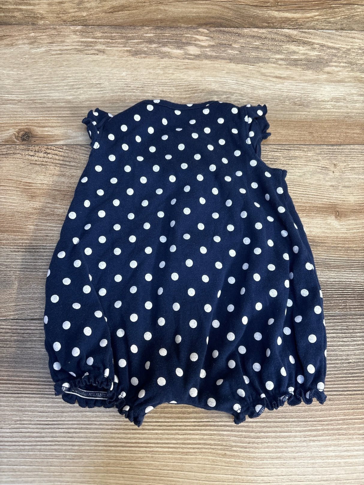 Navy blue baby romper with white polka dots on wood background