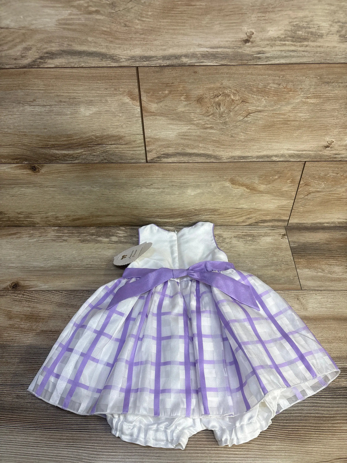 Front view of American Princess dress and bloomer shorts set with white bodice, purple plaid skirt, and sash on wood floor