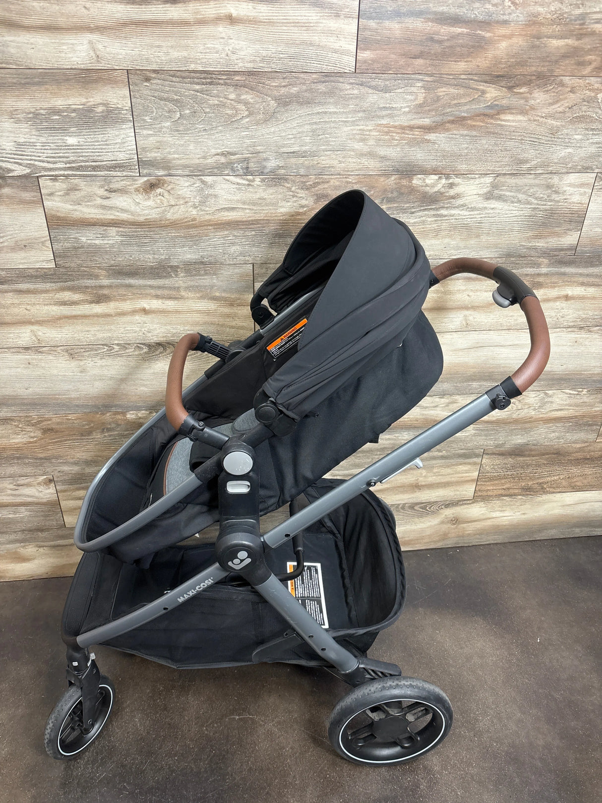 Black baby stroller with brown handle, large storage basket, and modern wheels on wood floor