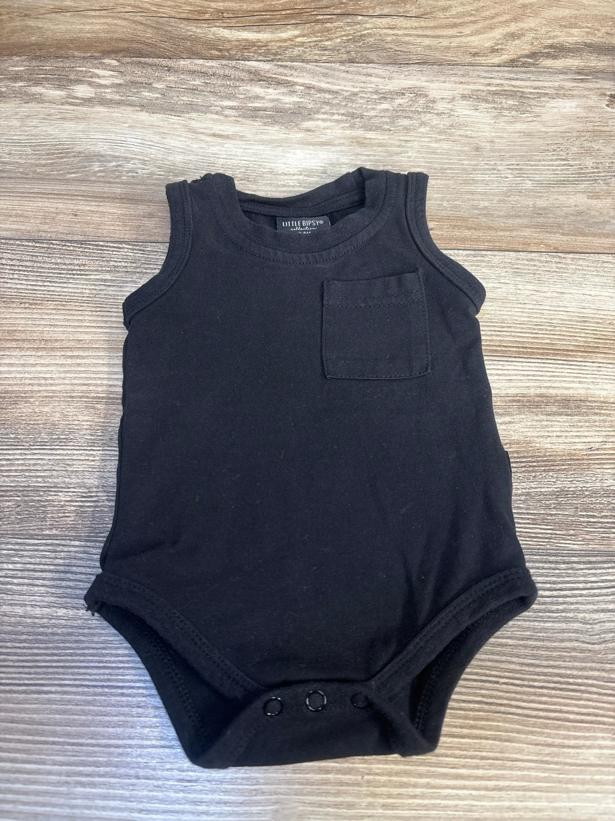 Black sleeveless baby bodysuit with chest pocket, snap closures, on wooden background