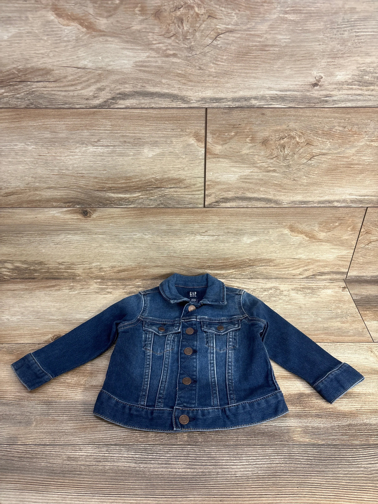 Kids blue denim jacket with large buttons laid flat on wooden floor background