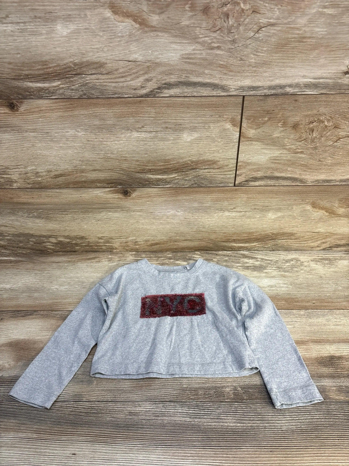 Gray long sleeve kids shirt with red NYC graphic, laid flat on wooden surface