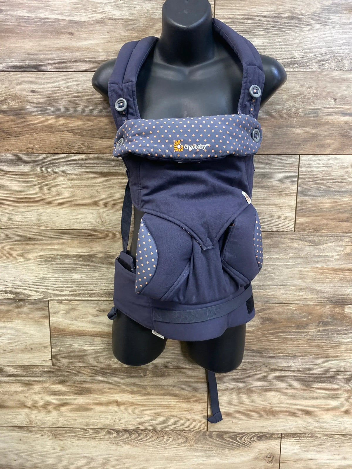 Front view of Ergobaby 360 carrier in dusty blue with padded straps, polka-dot headrest and ergonomic seat on wood background
