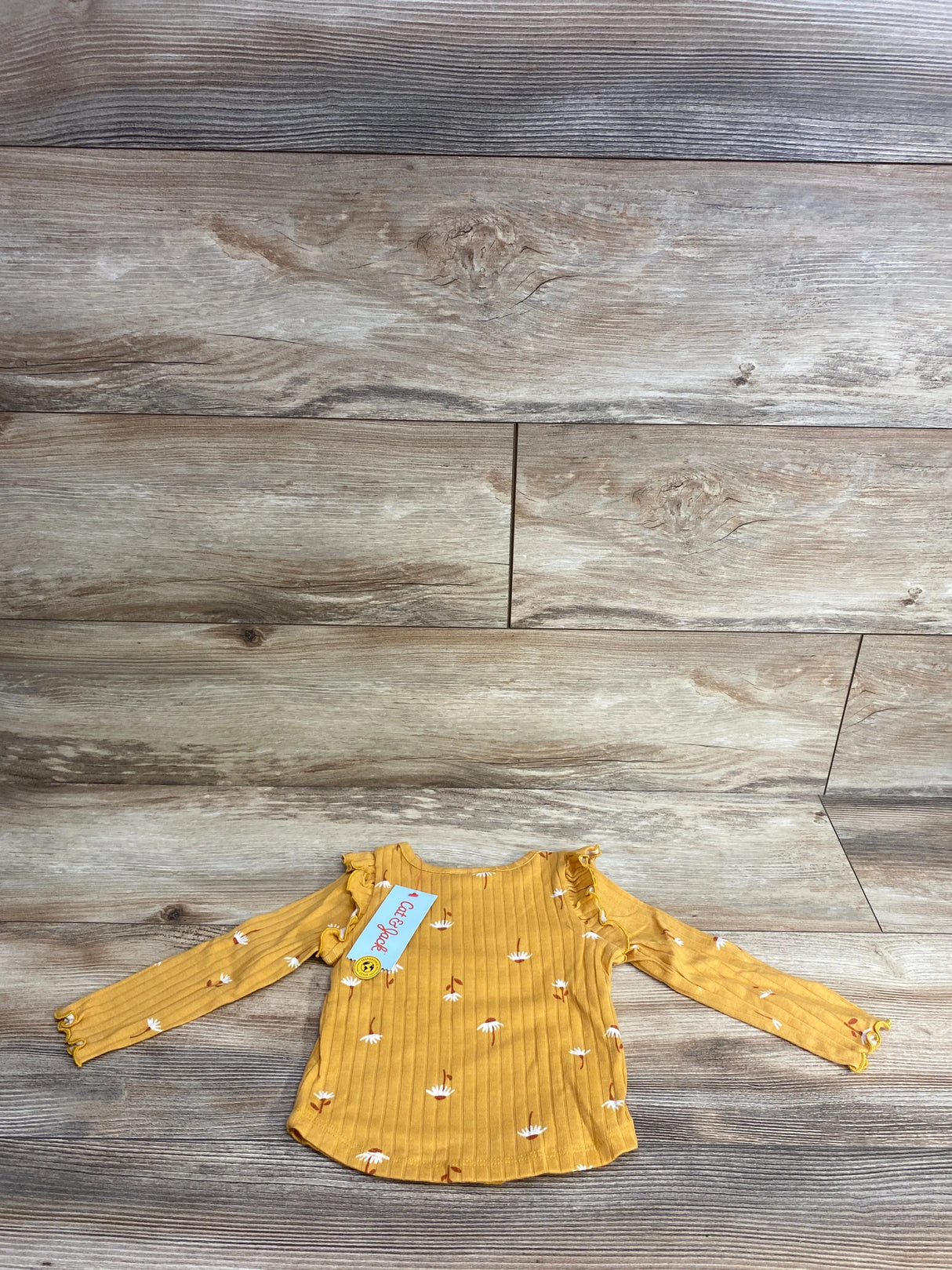 Mustard yellow long-sleeve toddler shirt with white floral print and ruffles on wooden floor