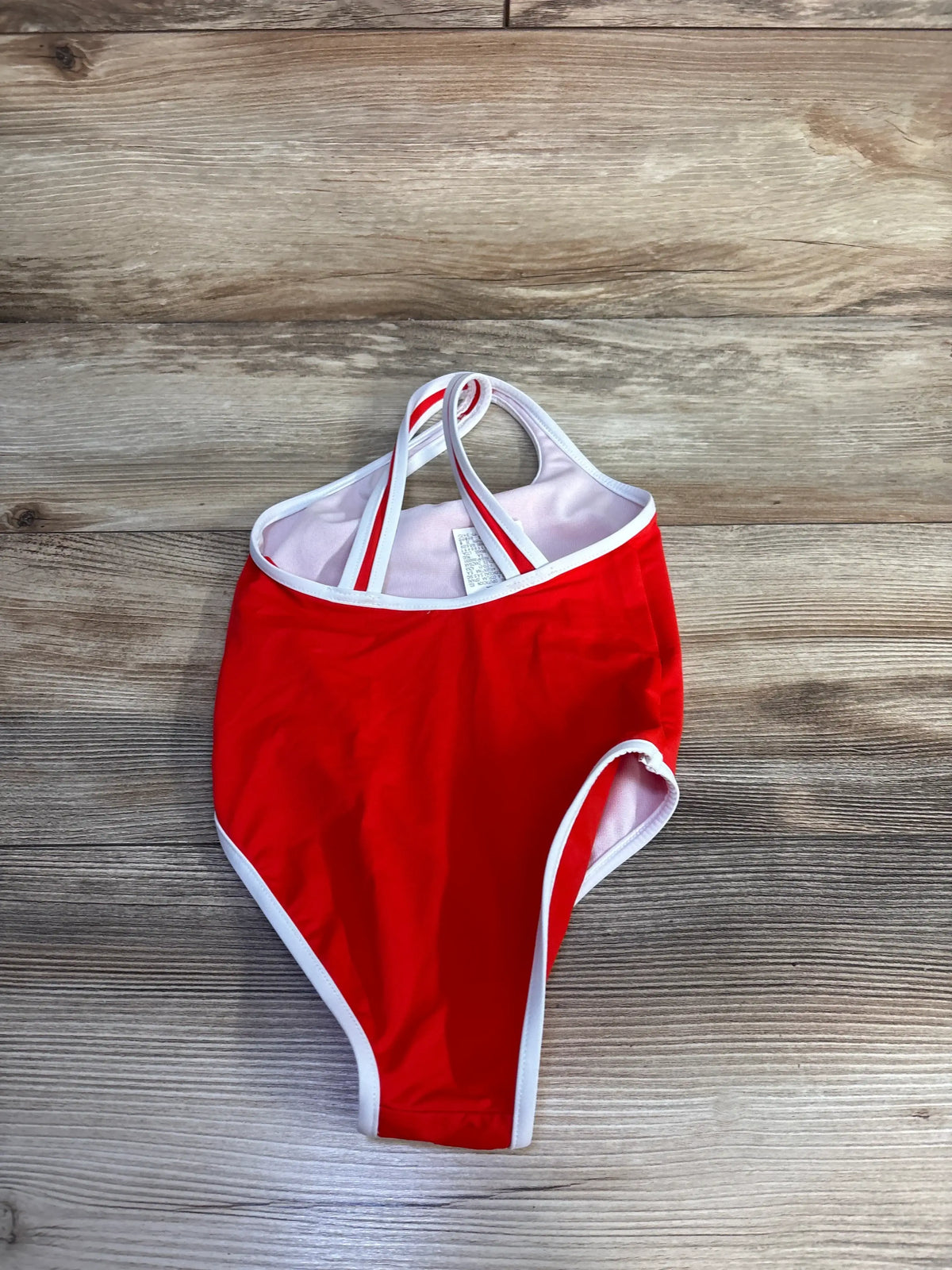 Top view of Zara red one-piece swimsuit showcasing white trim, shoulder straps, and pink lining on a wood-grain background