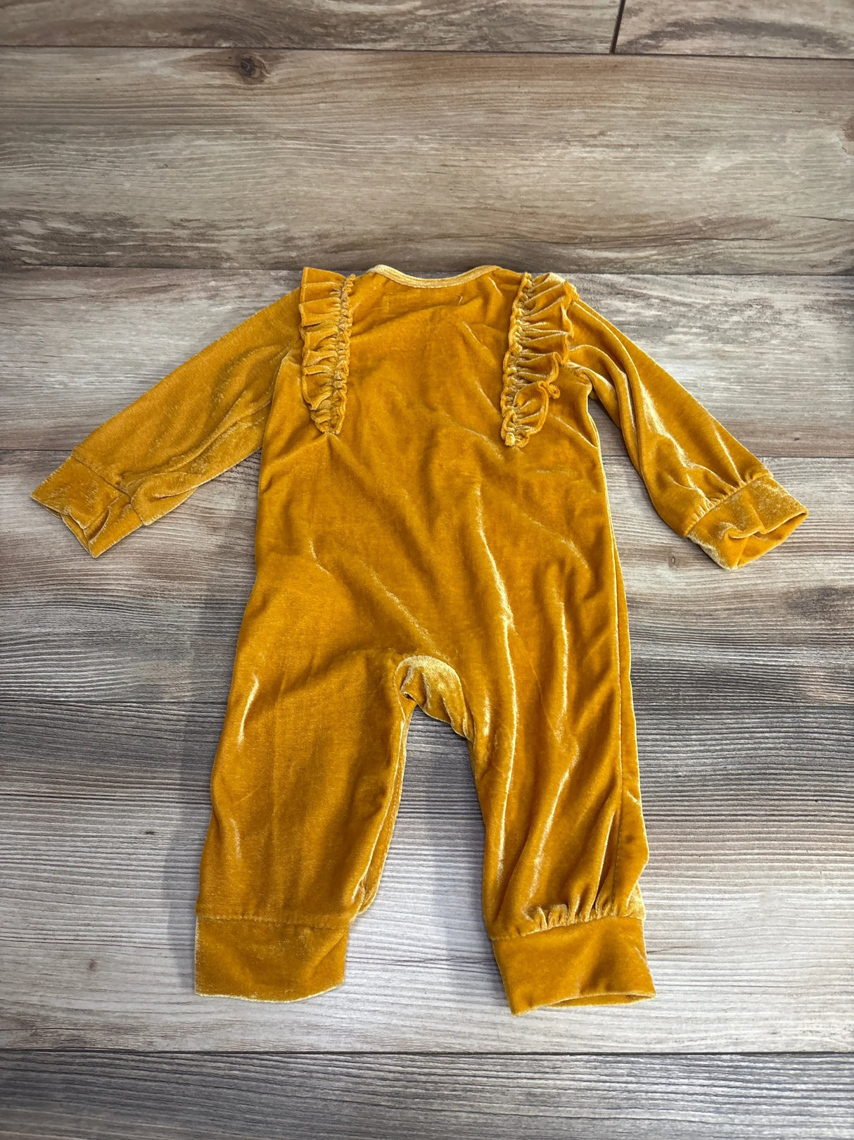 Yellow velvet baby romper with ruffle shoulders on wood background, long sleeves