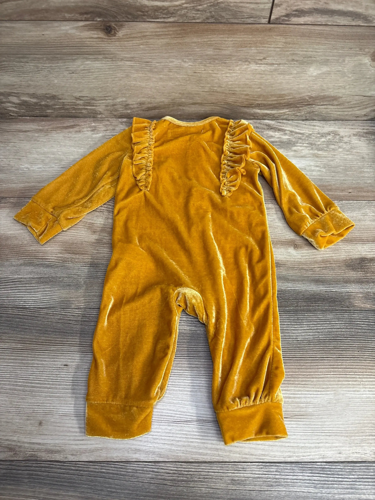 Yellow velvet baby romper with ruffle shoulders on wood background, long sleeves