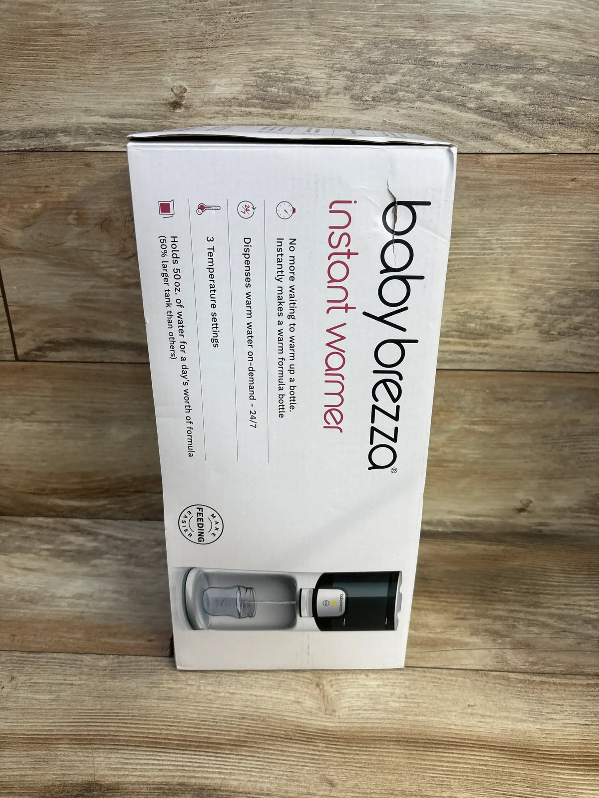 Front view of Baby Brezza Instant Baby Bottle Warmer box showing product image and 'instant warmer' branding on white box against wooden backdrop