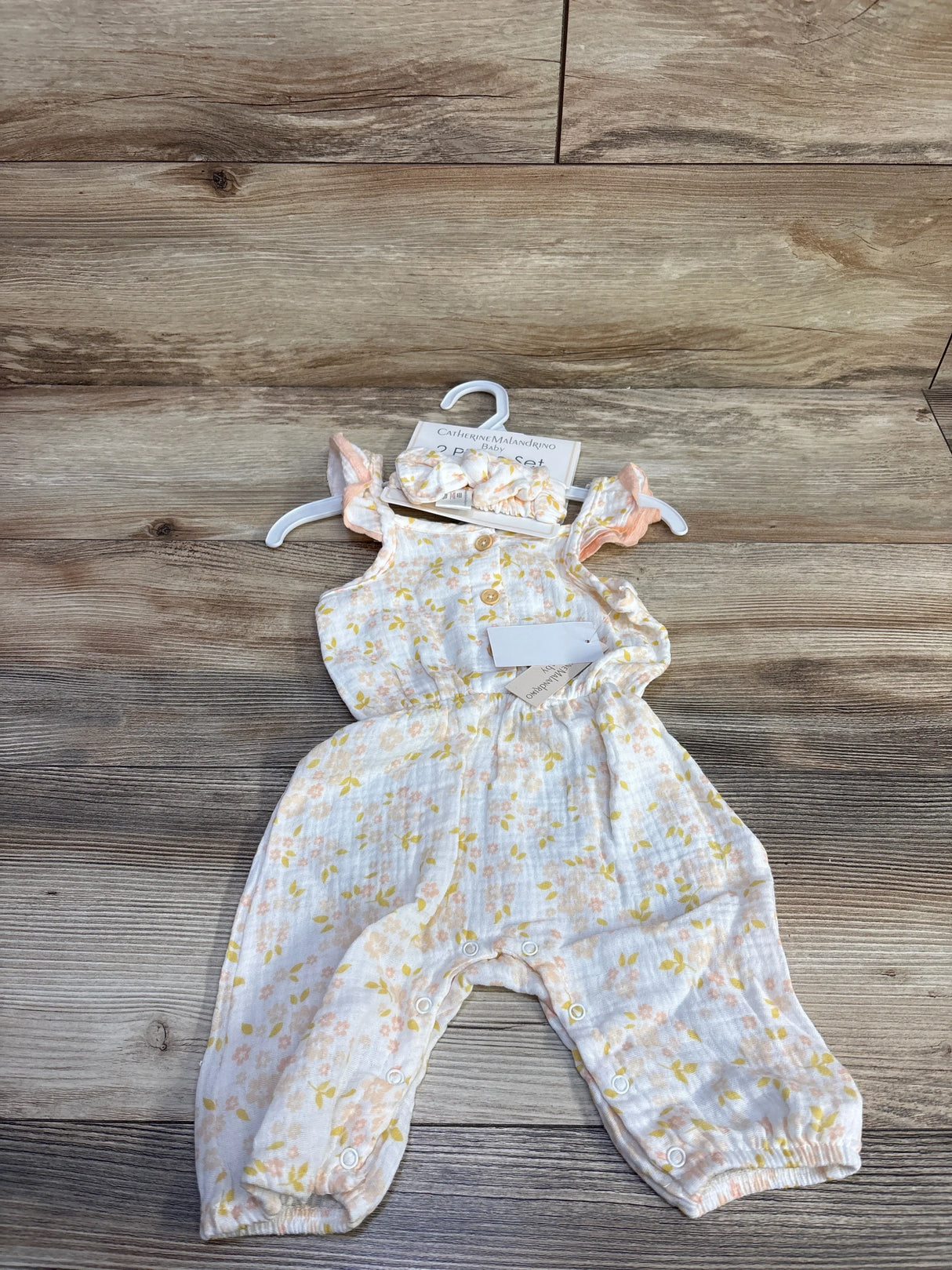 Flat-lay of newborn gauze jumpsuit with matching ruffle headband, pastel floral print, front buttons and leg snaps on wood