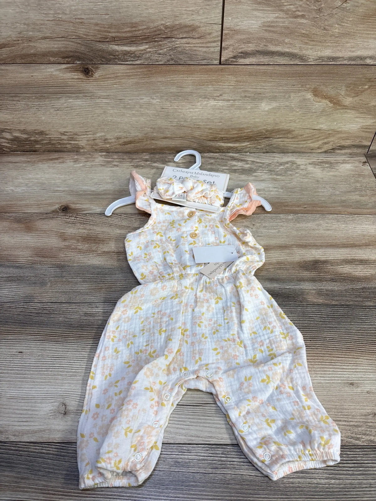 Front view of NWT Catherine Malandrino gauze jumpsuit in white with yellow floral print and matching headband on hanger on wood plank floor