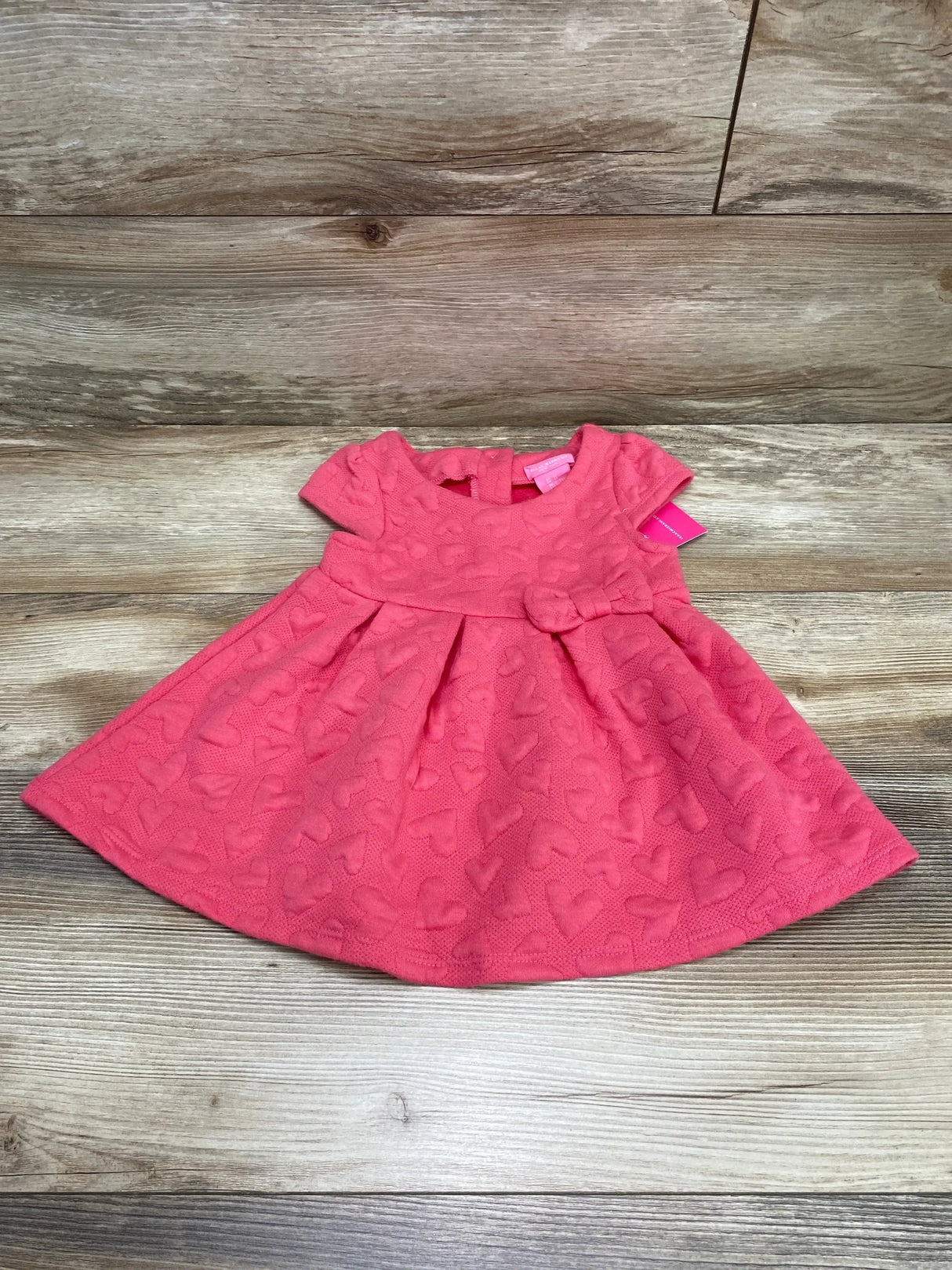 Front view of NWT Isaac Mizrahi dress in pink showcasing tonal quilted heart pattern with cap sleeves and bow waist on wood plank floor