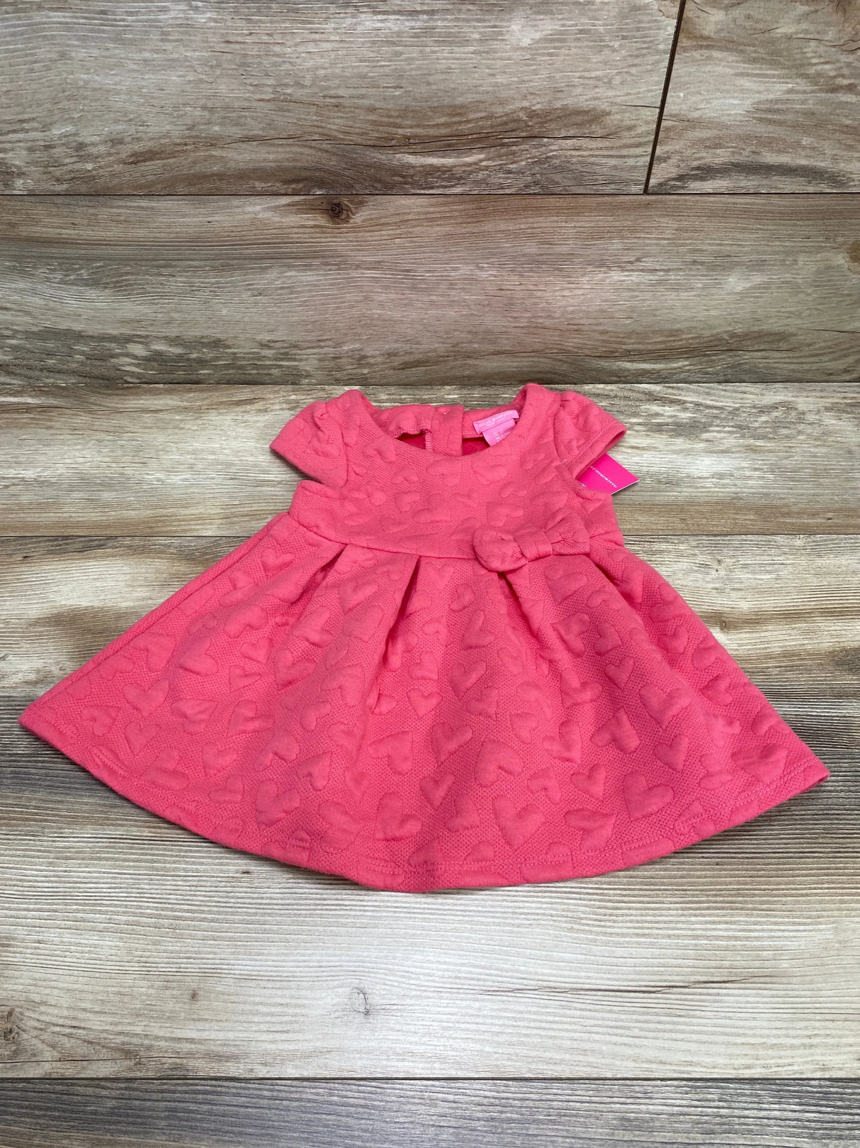 Flat lay of pink Isaac Mizrahi toddler dress size 3T showing quilted heart texture, short cap sleeves, waist bow on wood background
