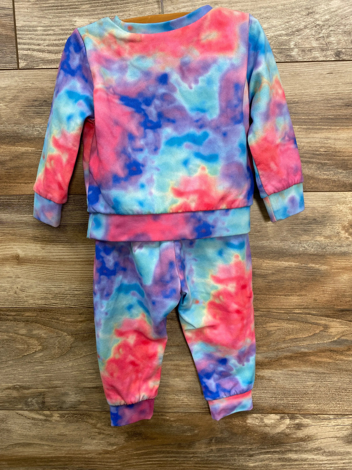 Colorful tie-dye kids sweatshirt and pants set in red, blue, purple, and teal on wooden background