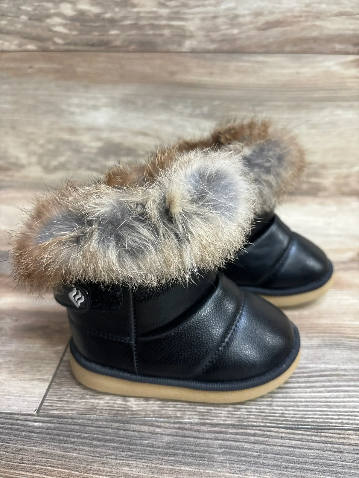 Black toddler boots with faux fur trim and rubber soles on wooden background