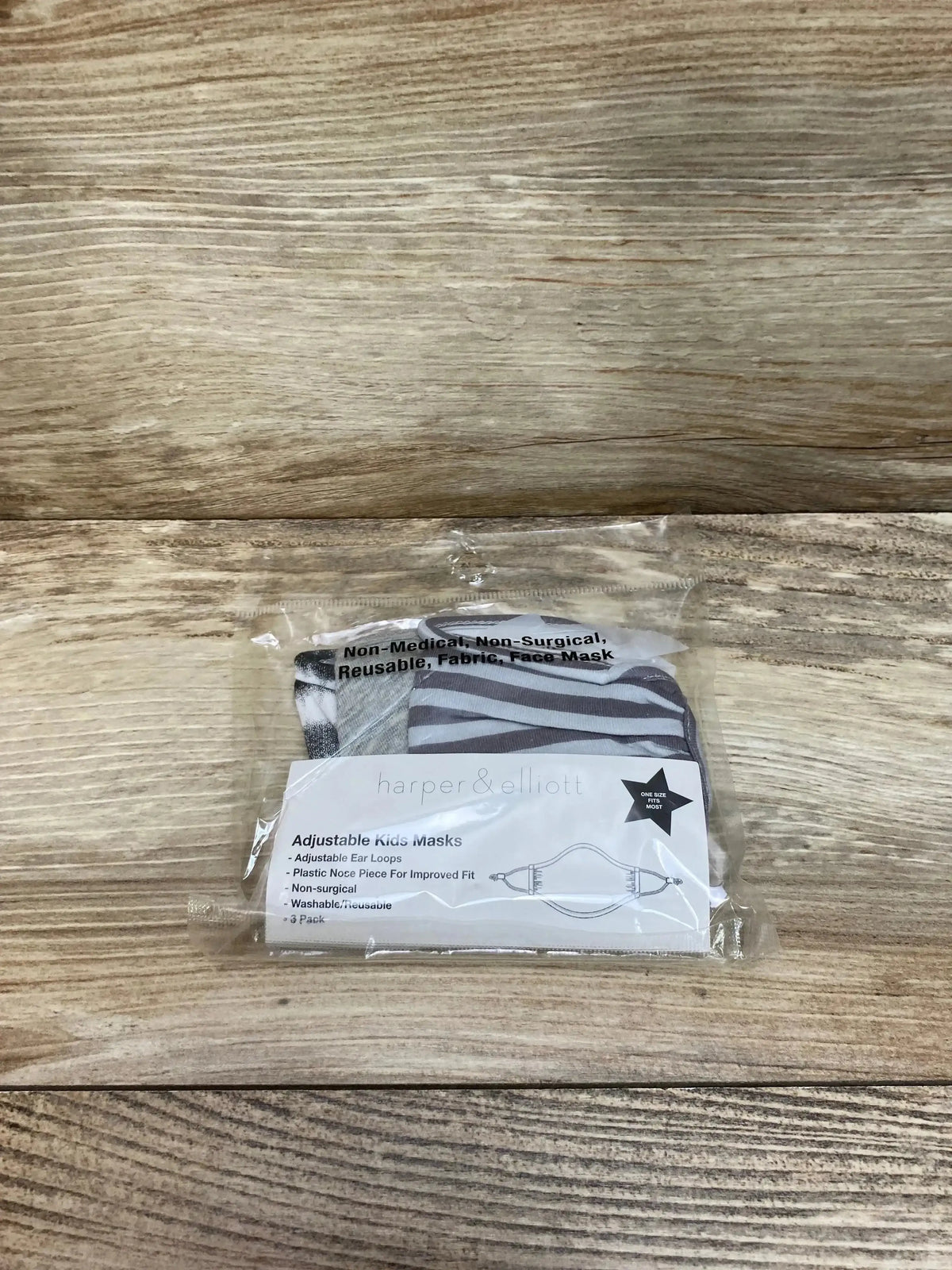 Front view of 3-pack grey kids face masks in clear plastic packaging showing striped and solid designs and label on wood background