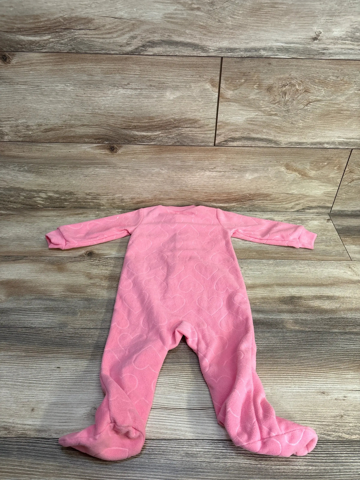 Back view of Carter's pink 9m footed blanket sleeper showcasing embossed heart pattern on fleece, laid flat on wood plank background