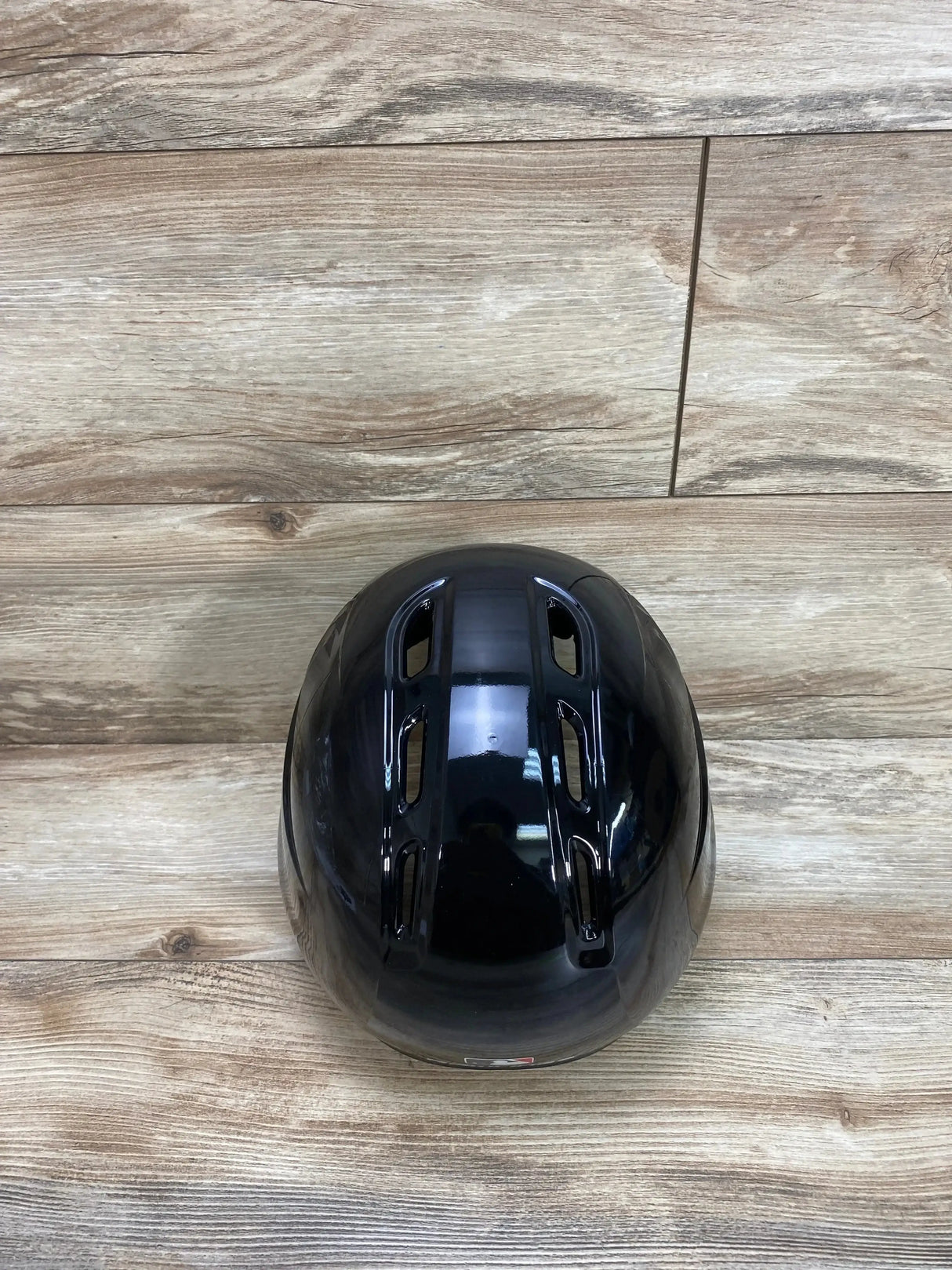 Top-down view of Rawlings black batting helmet showing glossy finish and ventilation slots on a wood floor background