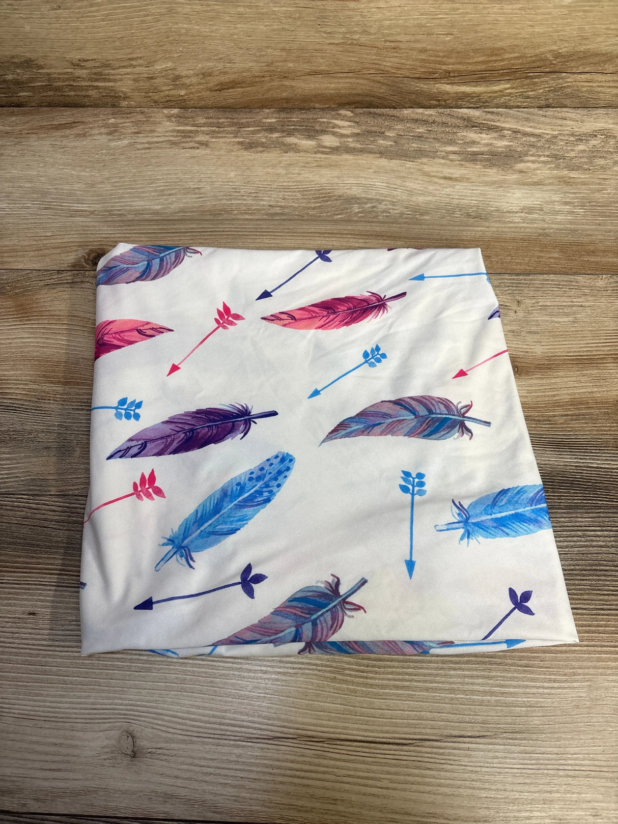 Folded fabric with colorful feather and arrow pattern on a wooden surface