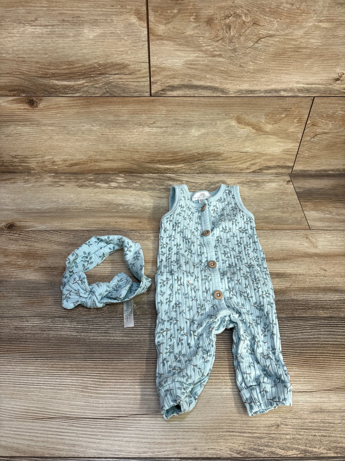 Front view of Willow + Whimsy blue ribbed jumpsuit and matching headband showcasing button front and floral pattern on wood floor