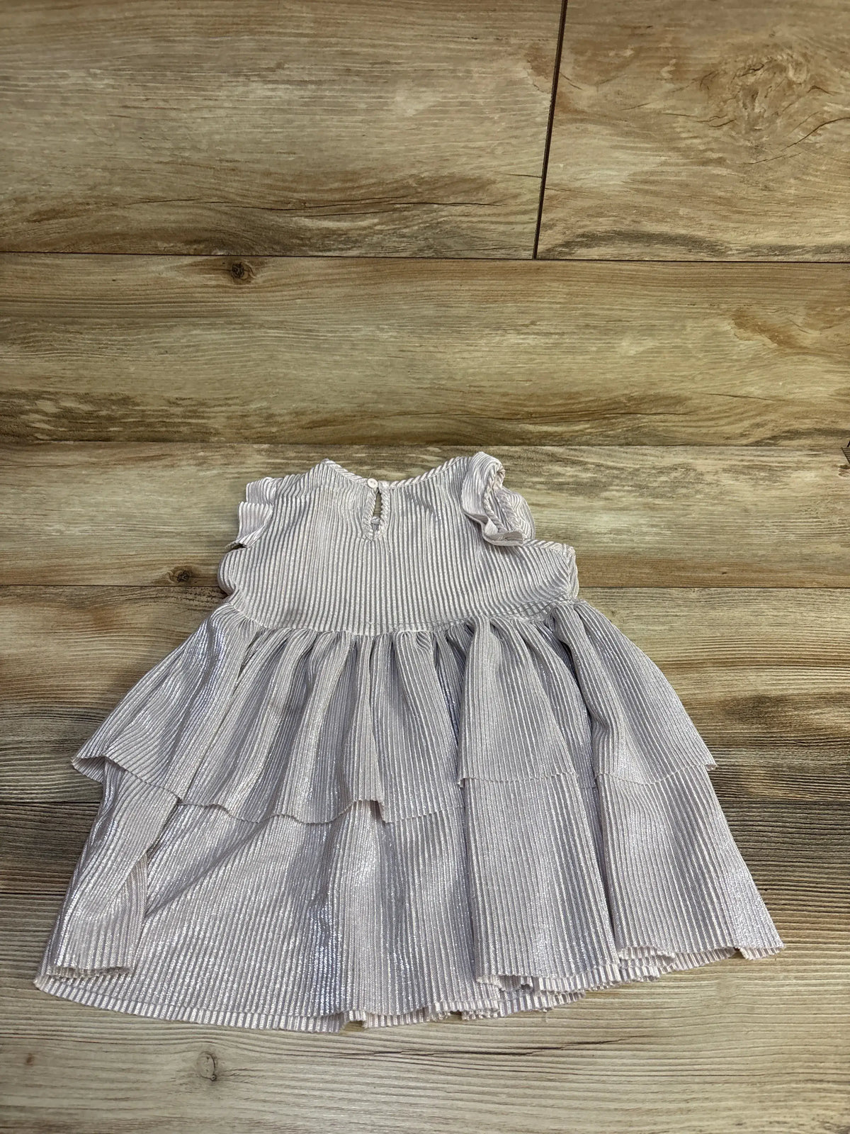 Flat lay of silver metallic layered toddler dress with ruffled cap sleeves, tiered pleats, and back button on wood background