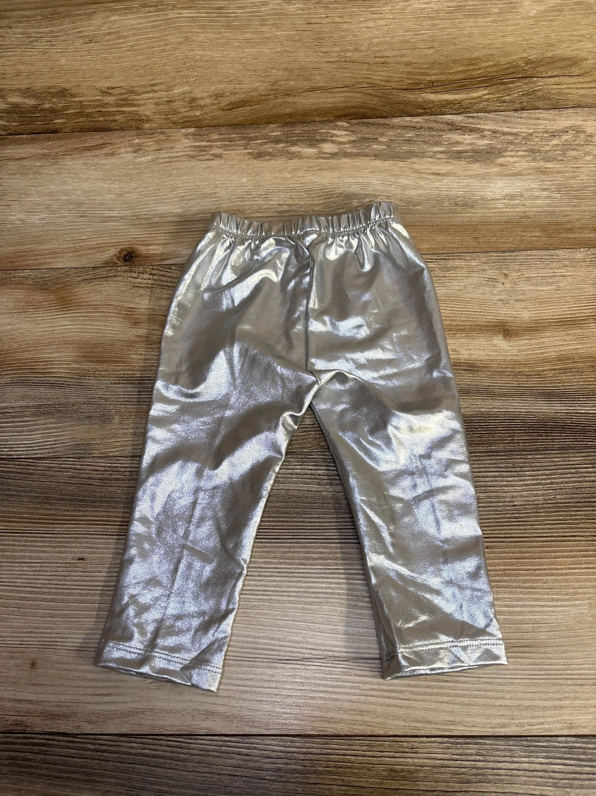 Metallic silver pants for kids displayed on a wooden floor background