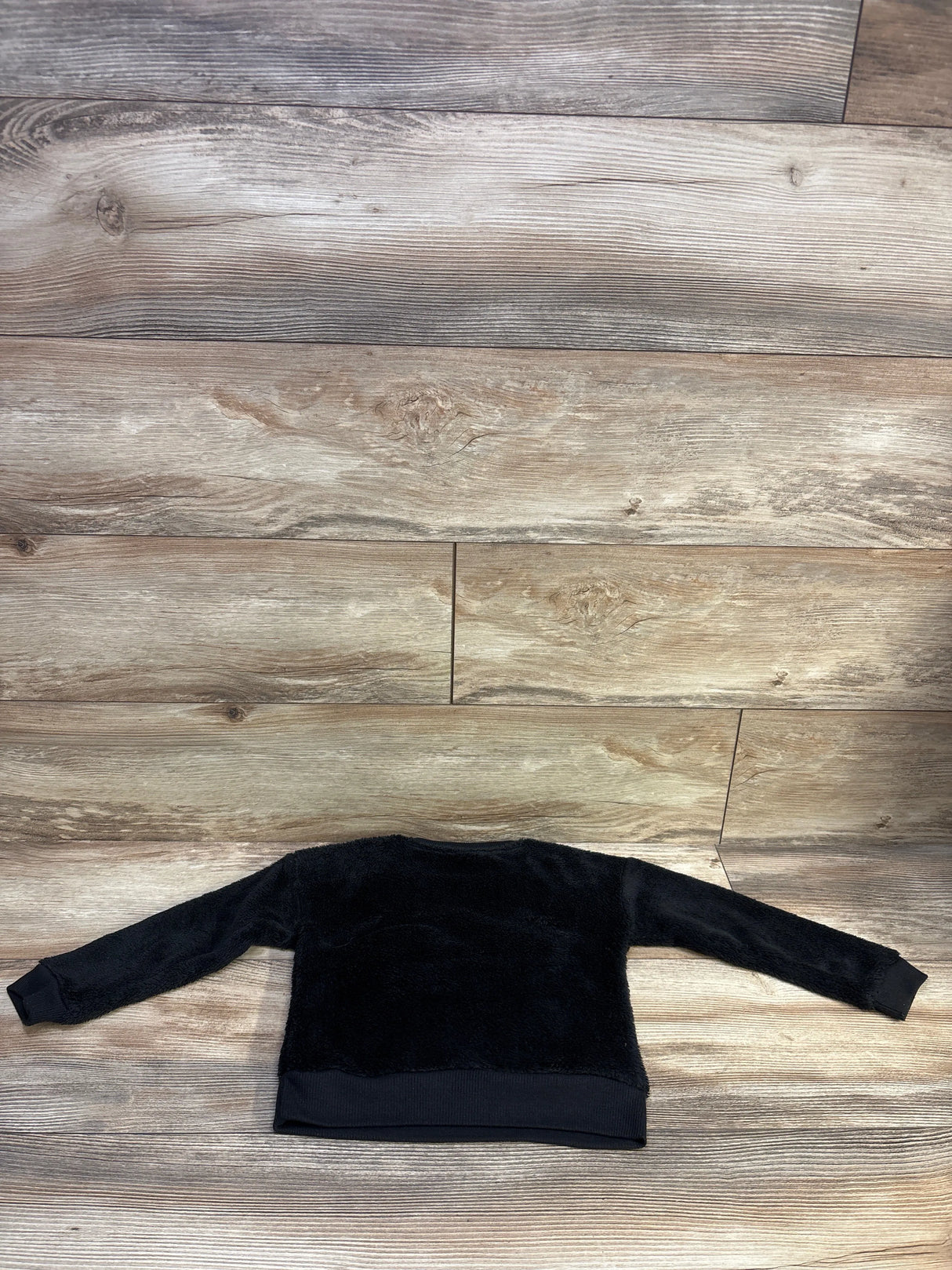Back view of black Mickey Mouse pullover sweatshirt in plush fleece with ribbed cuffs, laid flat on wood background, size 3T