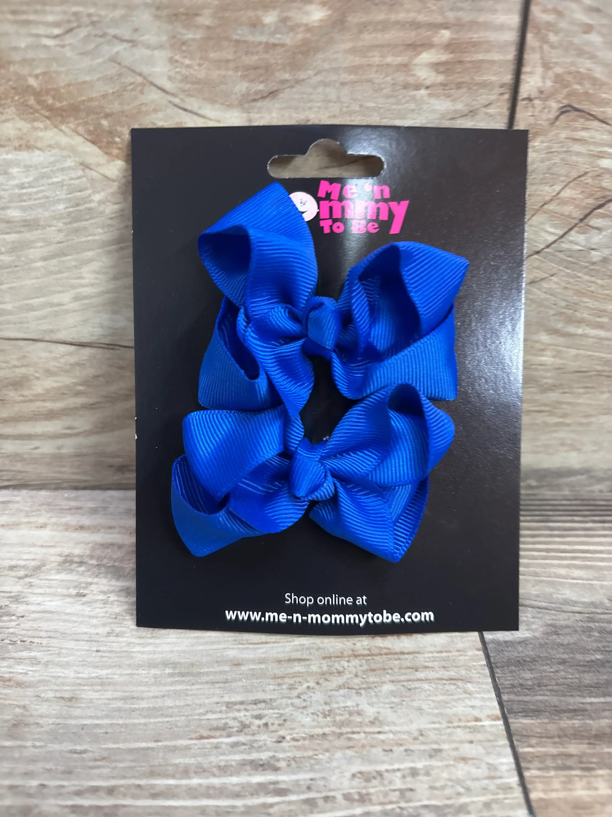 Two bright blue grosgrain hair bows on a Me n Mommy To Be display card.