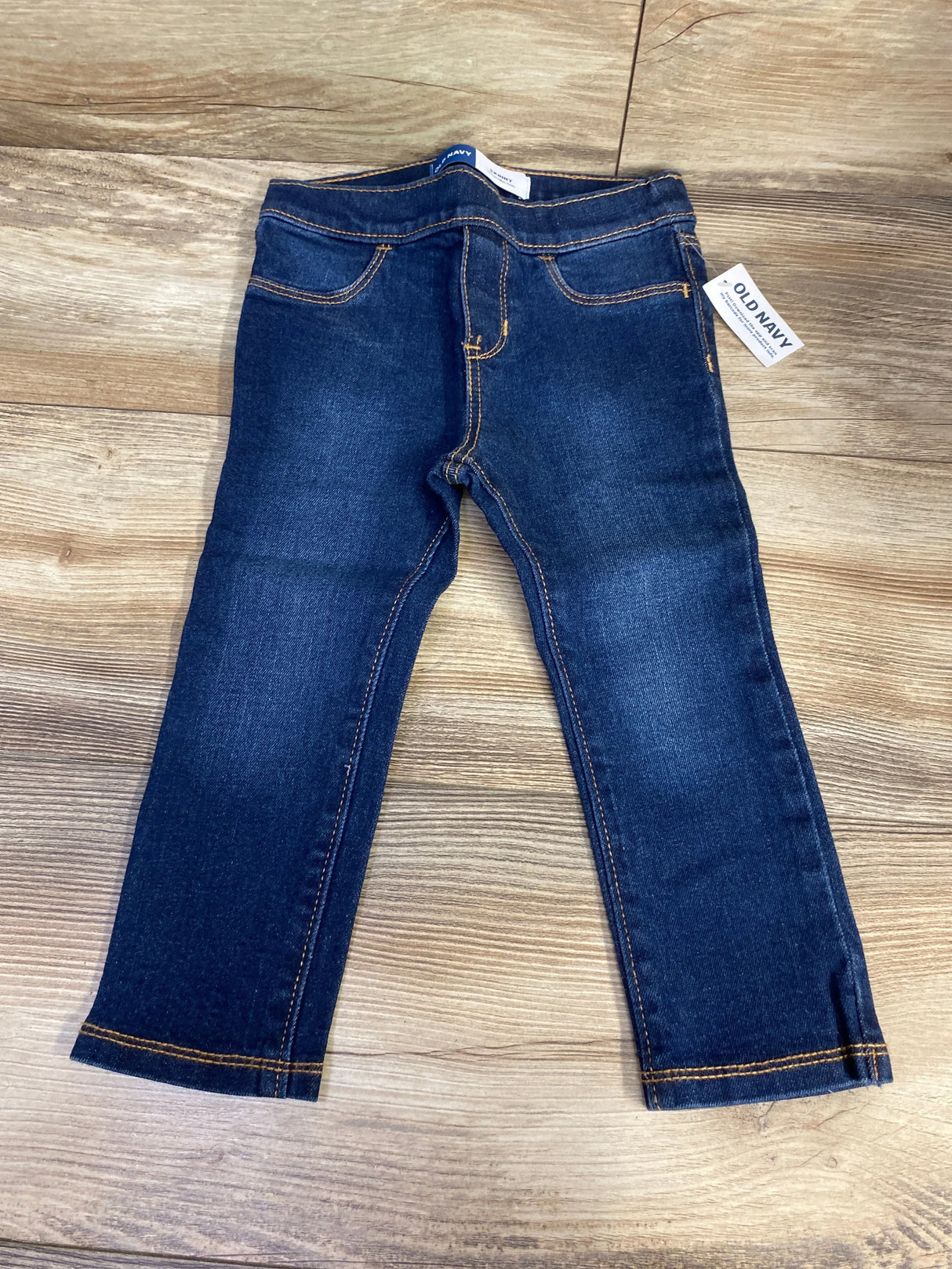 Dark wash kids jeans with yellow stitching and Old Navy tag on wood floor