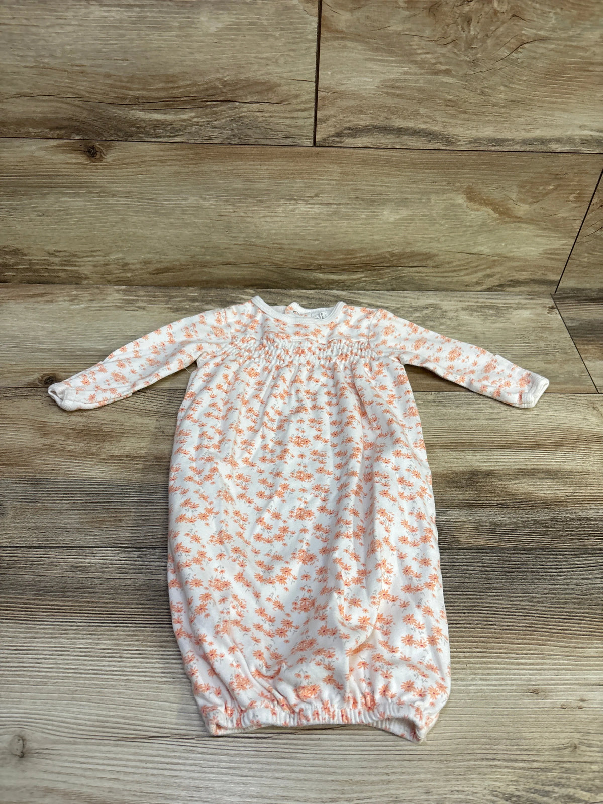 Front view of white floral baby sleep gown showcasing long sleeves and elasticized hem on a wood-look background