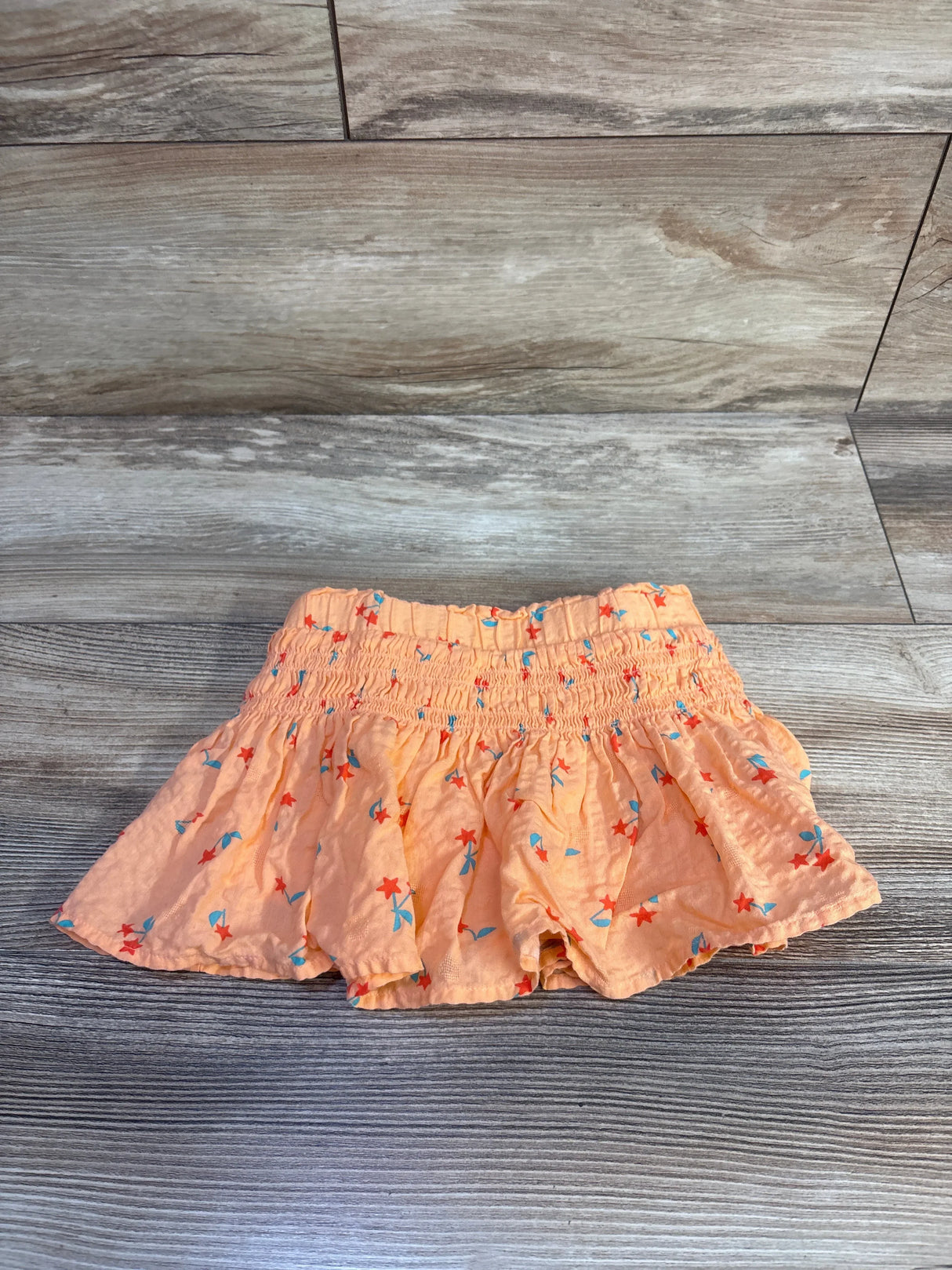 Flat lay of Cat and Jack orange toddler smocked skort with blue and red floral print and ruffled hem on light wood background