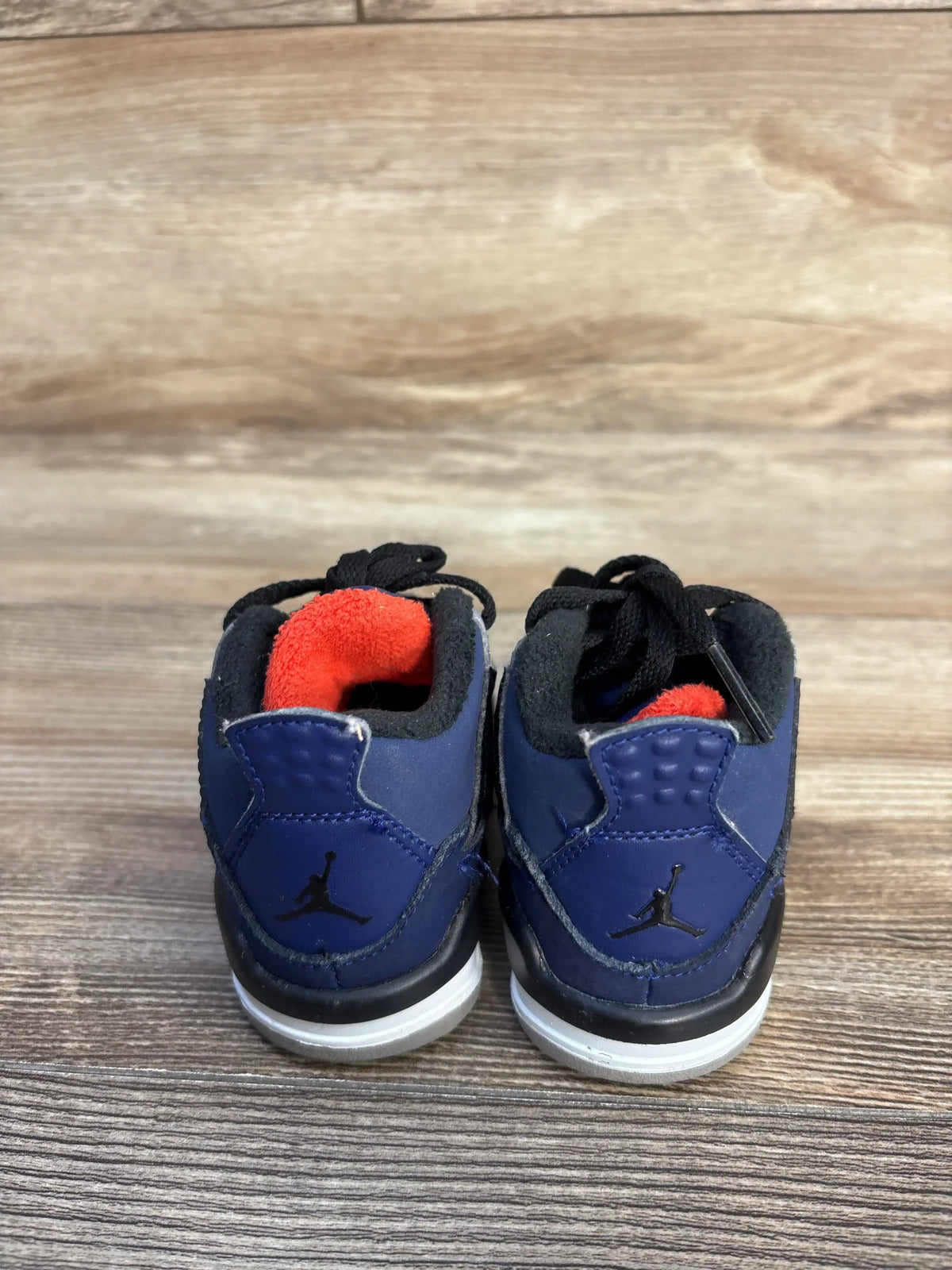 Rear view of Air Jordan 4 Retro TD toddler sneakers showcasing Loyal Blue uppers and red lining on a wood-grain background