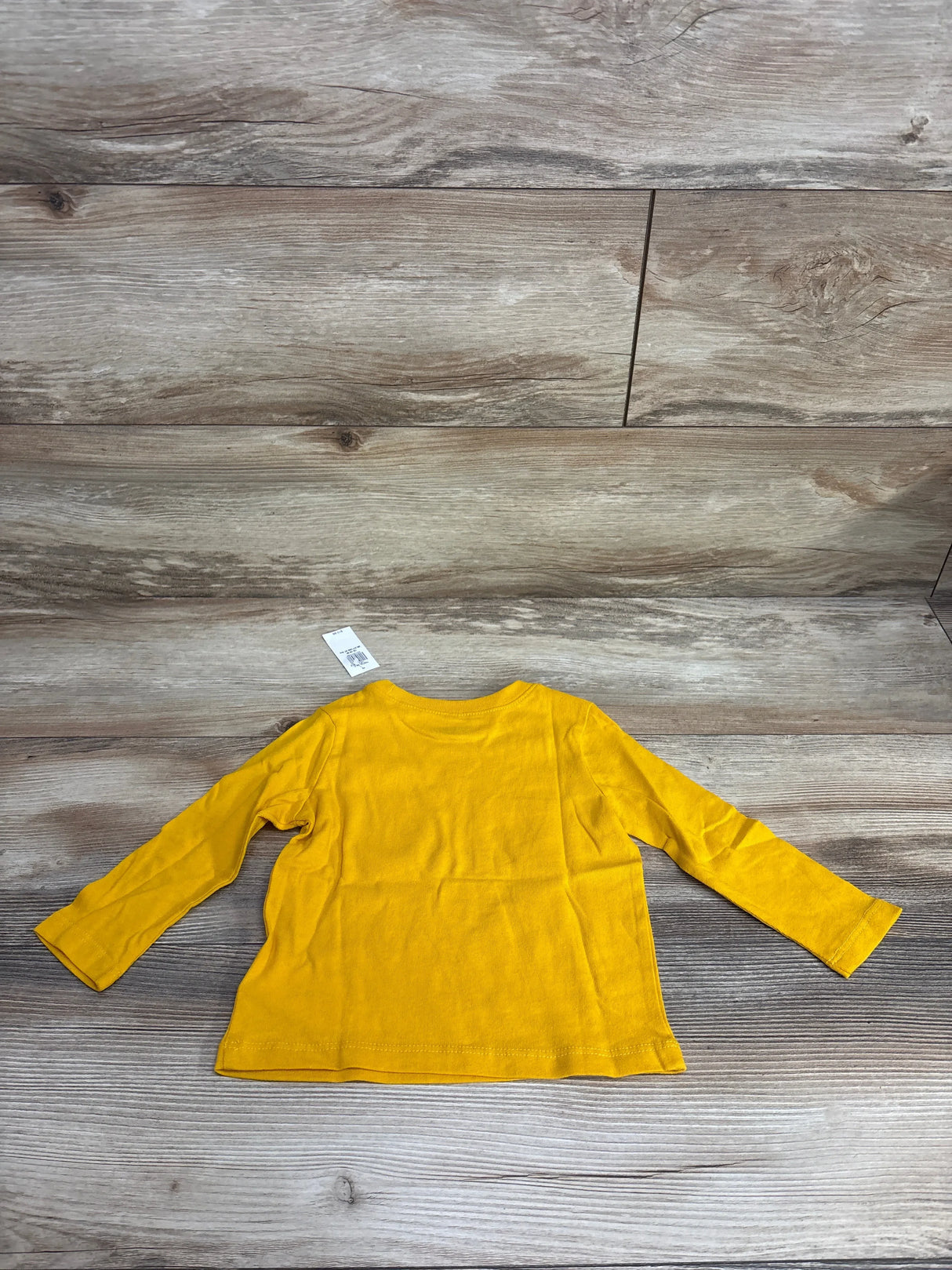 Back view of Old Navy yellow long-sleeve toddler shirt size 12-18M showing plain back and attached size tag on wood floor background