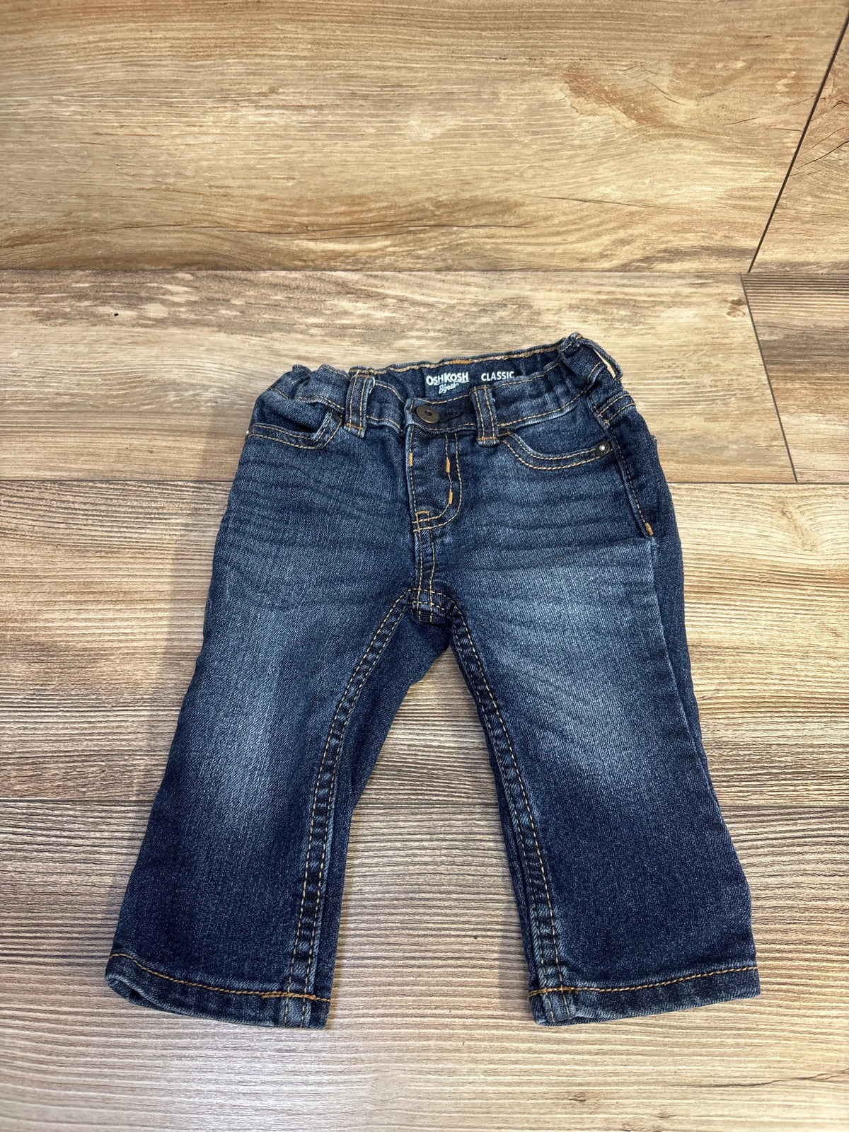 Front view of OshKosh Classic blue jeans, size 6 months, with belt loops, front pockets, button fly, and contrast stitching