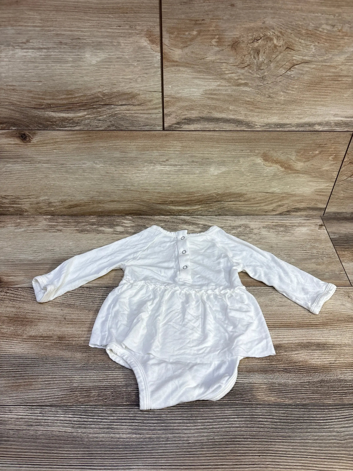 Flat lay of Spearmint Love white bamboo long sleeve bodysuit dress with gathered skirt and back snaps on wood background