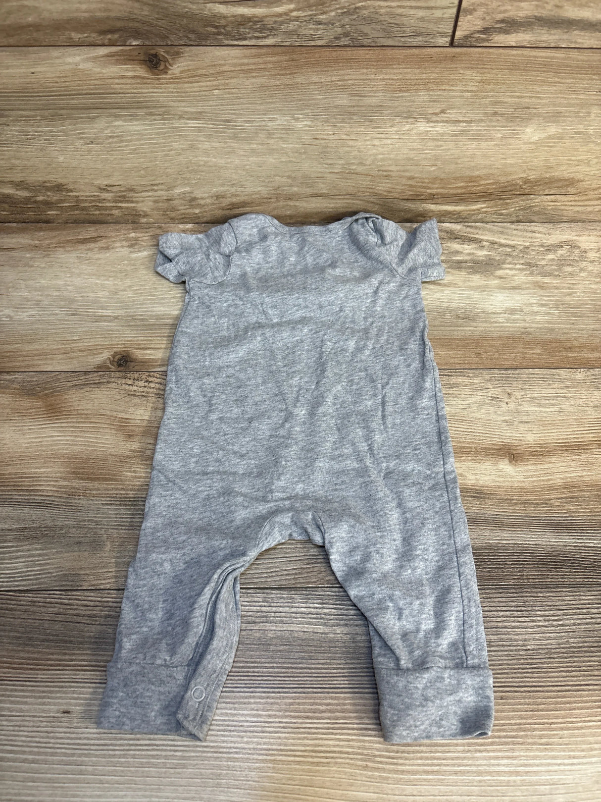 Top-down view of grey Okie Dokie Some Bunny Loves You jumpsuit size 3M showcasing ruffled cap sleeves and snap leg closure on wood floor