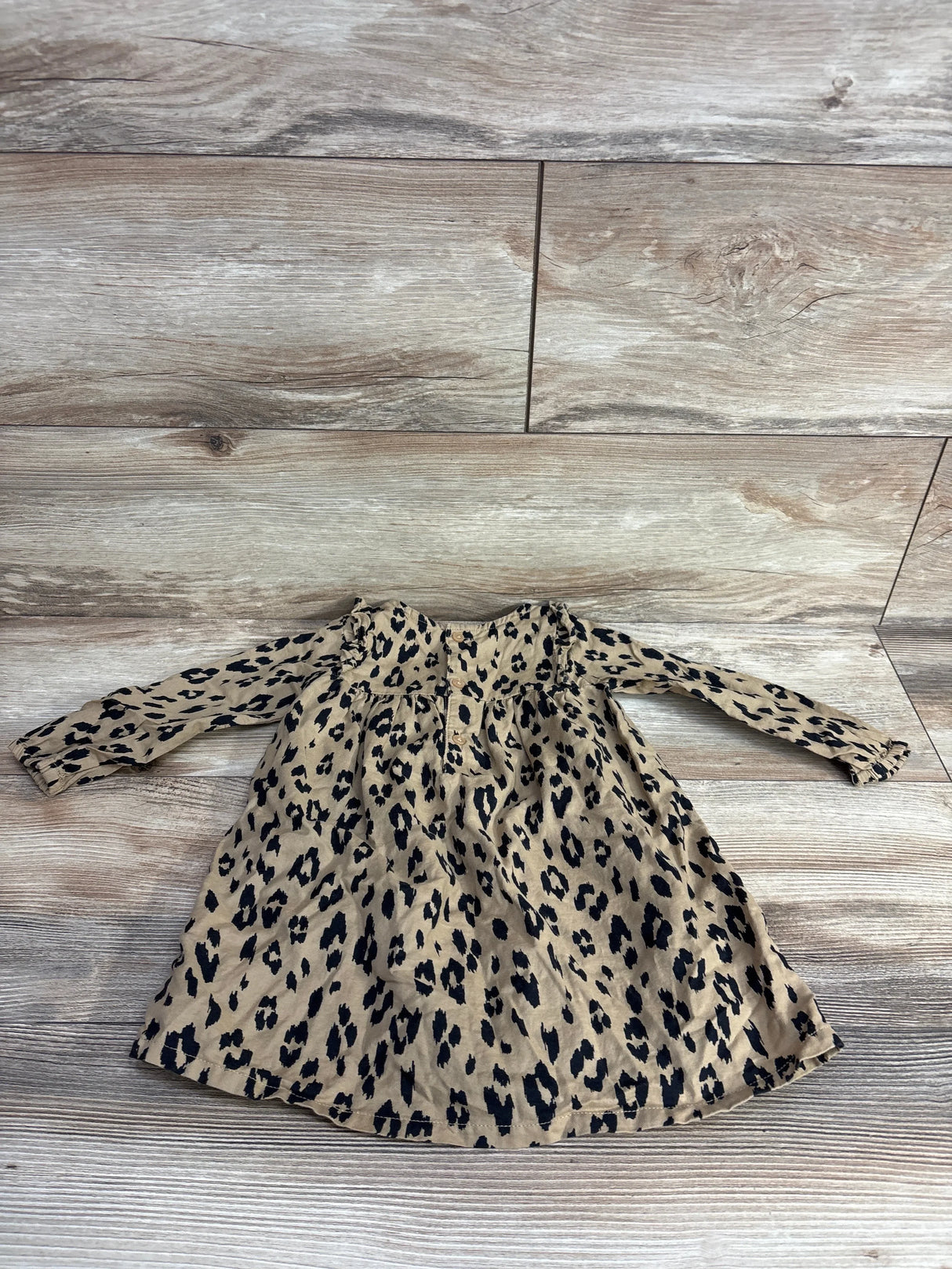 Long sleeve baby dress with tan and black leopard print pattern on wood background