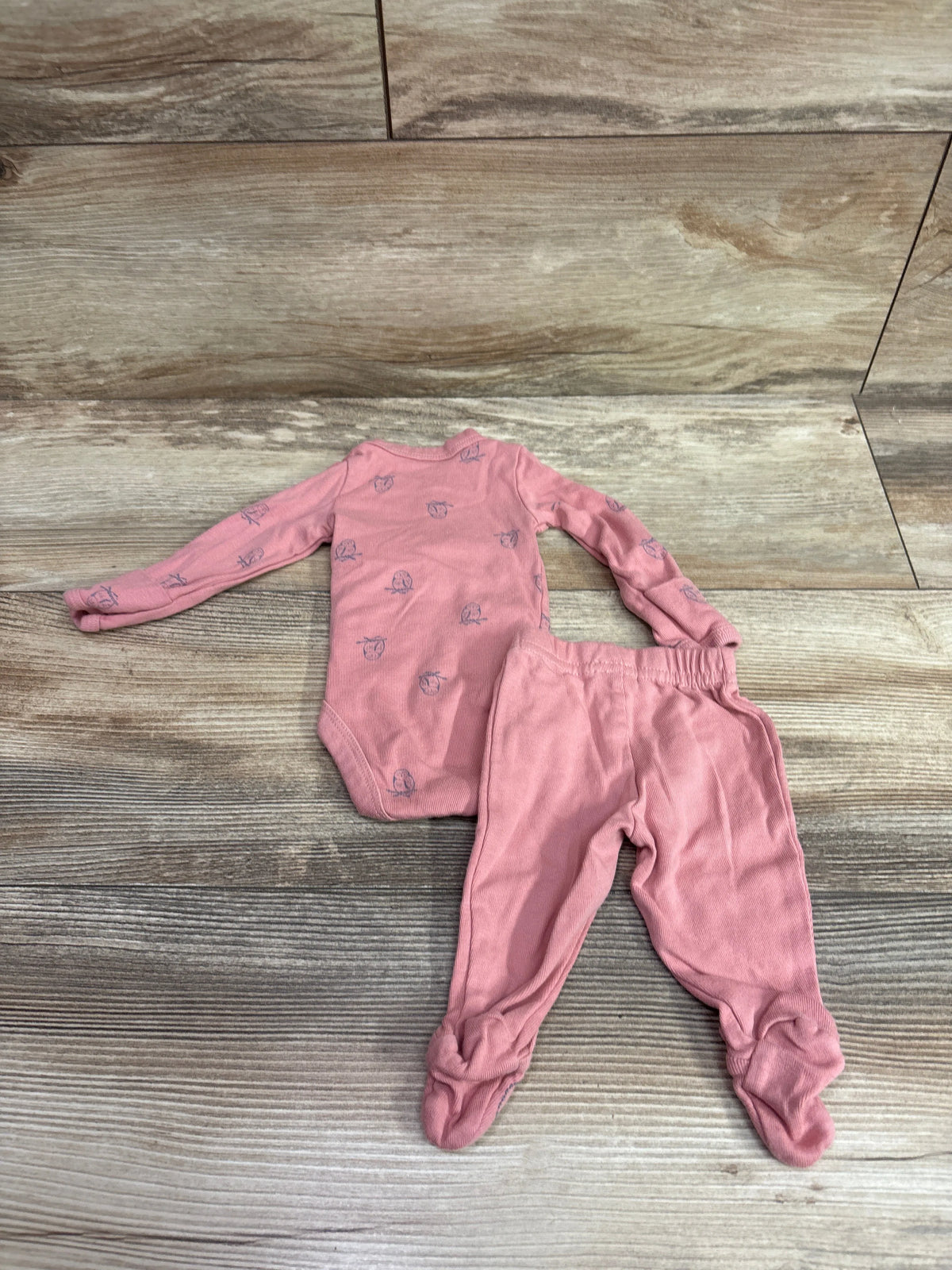 Top view of pink kimono bodysuit and footed pants set showcasing long sleeves and covered feet on a wood-look background